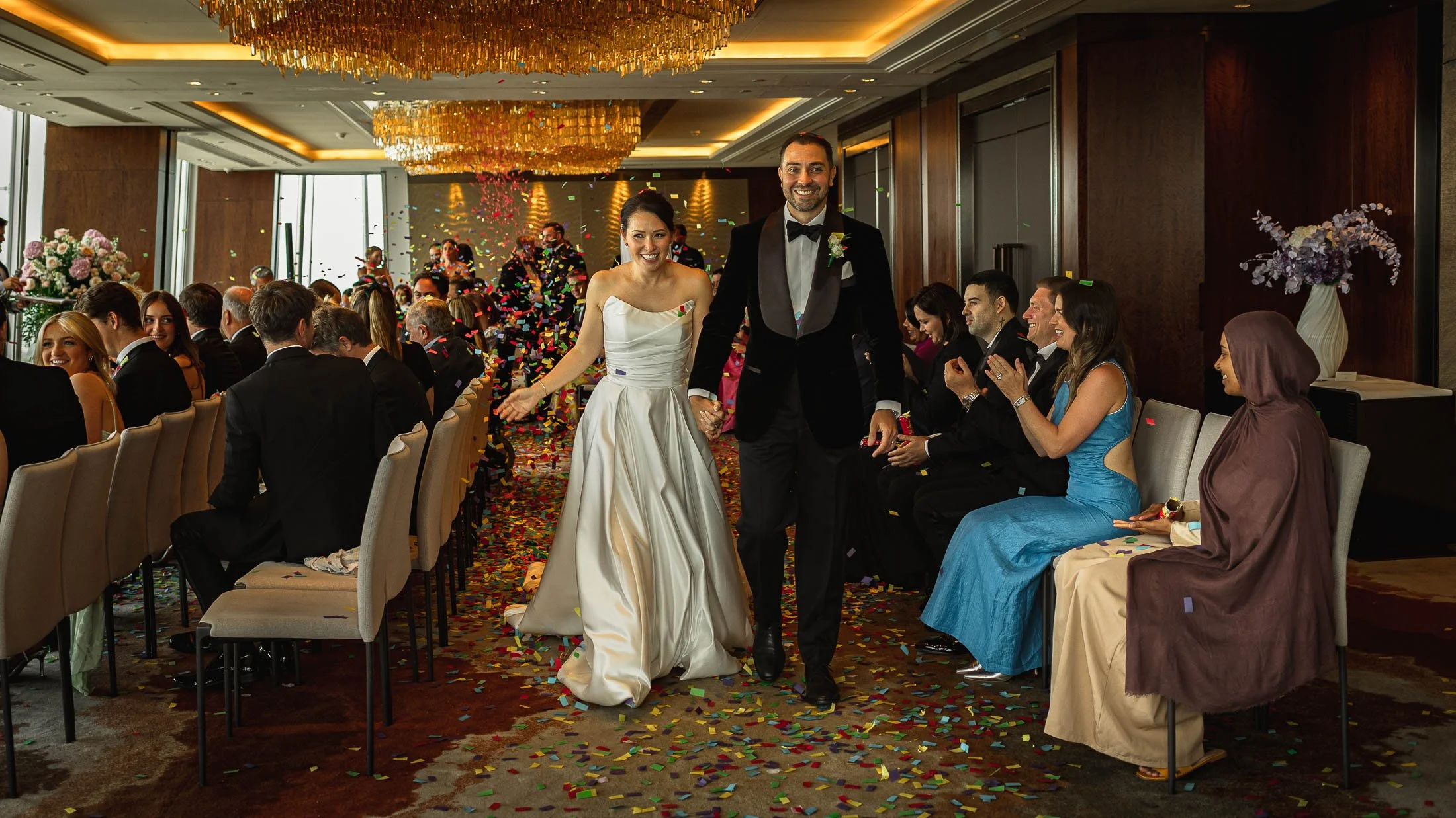 A bride and groom laughing together as they are covered in confetti exiting their indoor London wedding ceremony at The Shard.