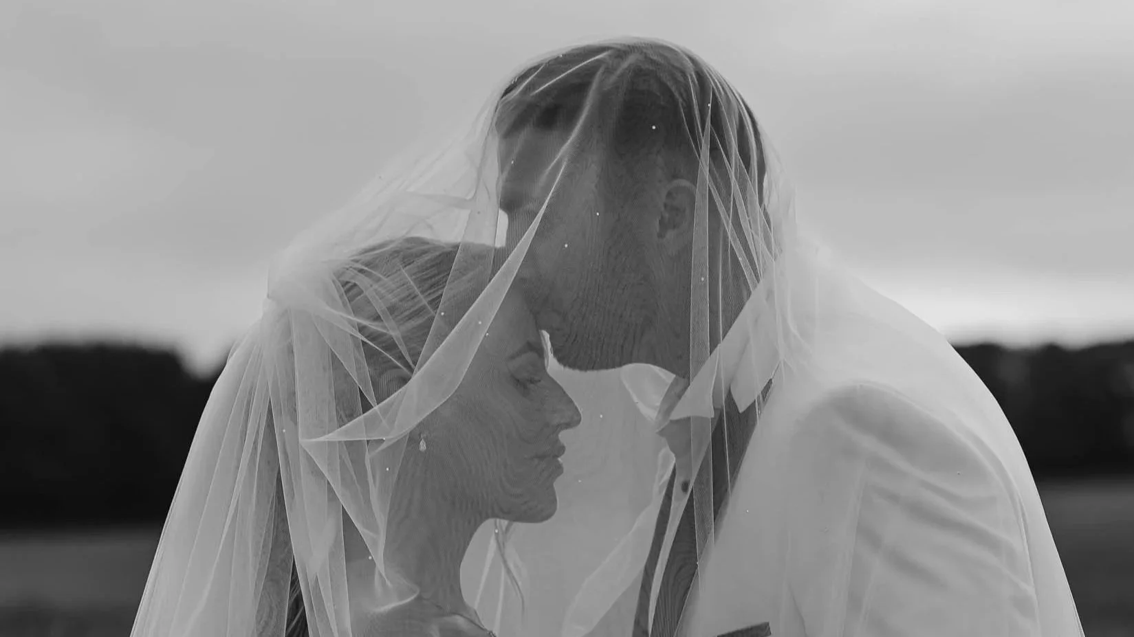 groom kisses brides forehead as they stand underneath a veil.