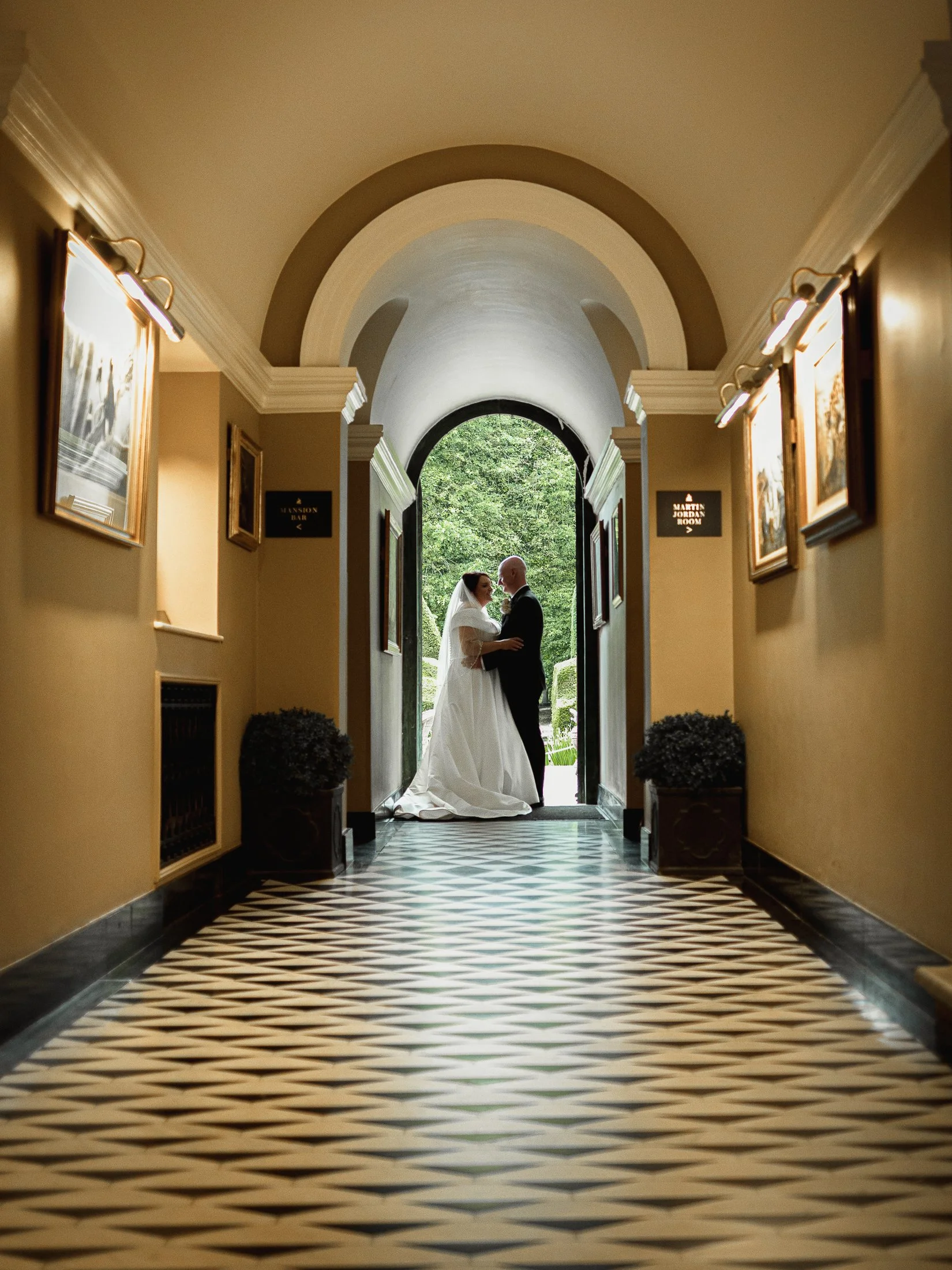 Bride and groom stand underneath an archway at the end of the main corridor at Port Lympne Hotel & Reserve.