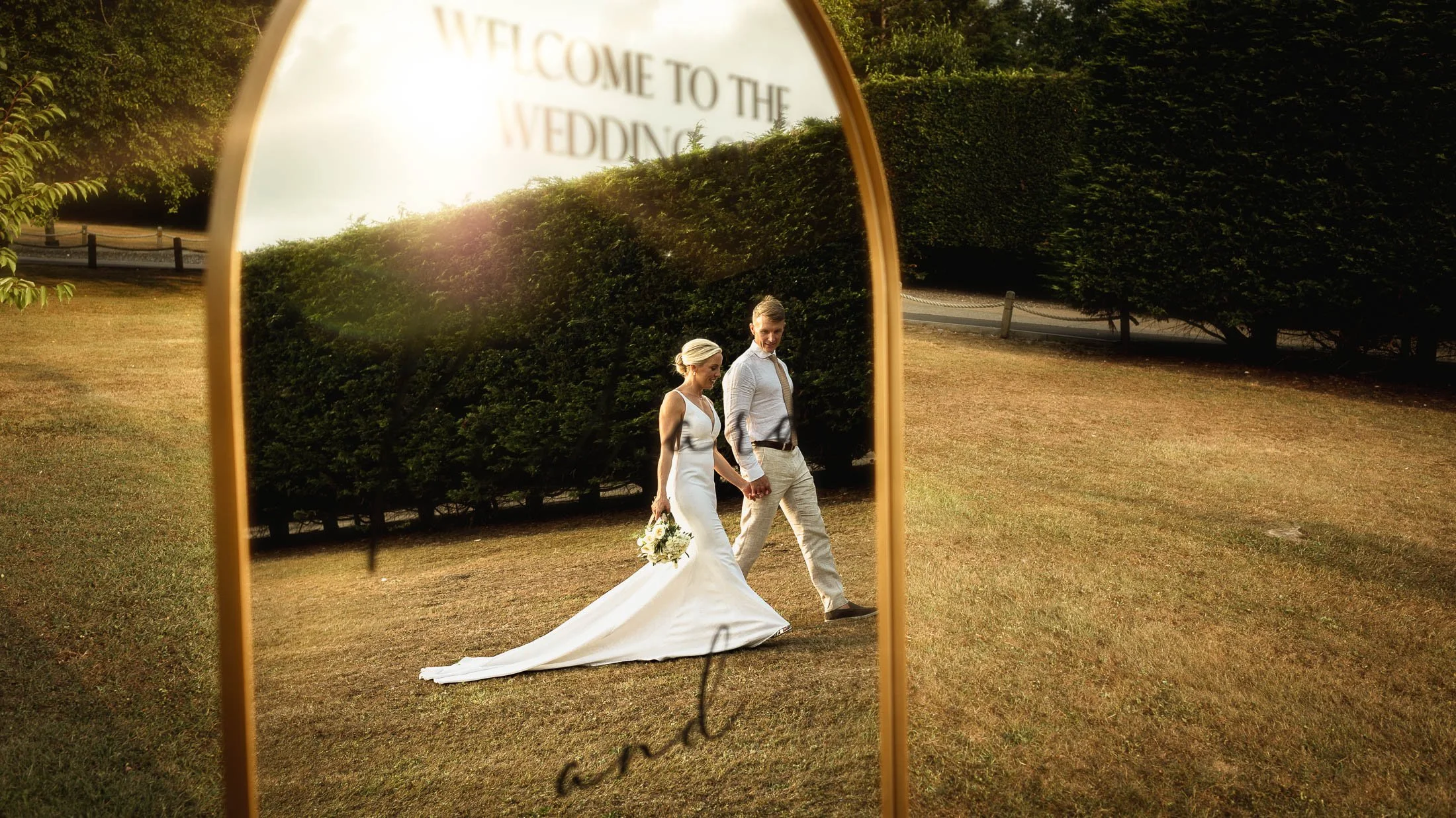 A bride and groom are caught in the reflection of a mirror as they walk through the grounds of Winters Barns  during golden hour on their summer wedding day.