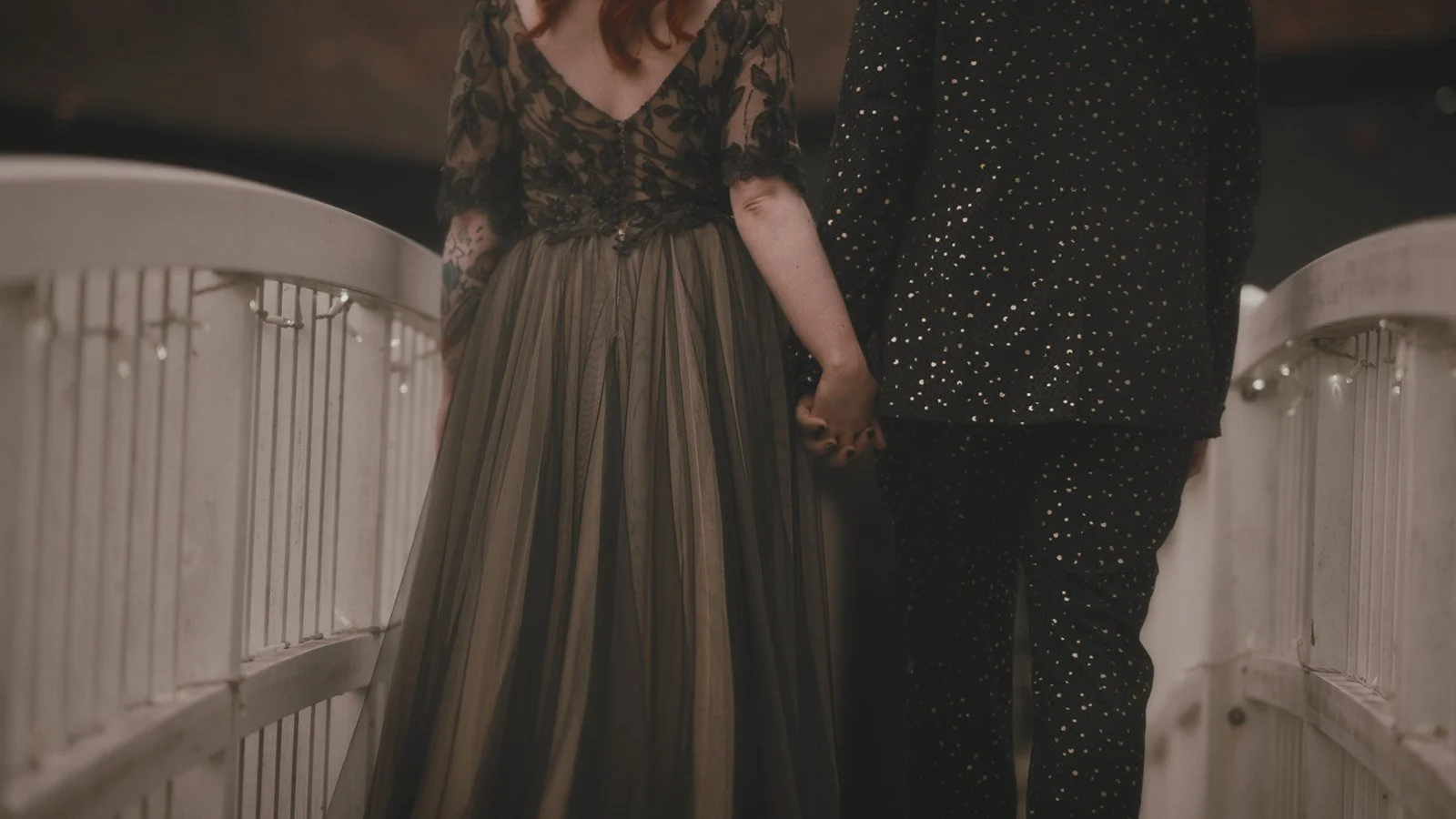 A gothic couple hold hands on the white bridge in the courtyard of Winters Barns, Canterbury.