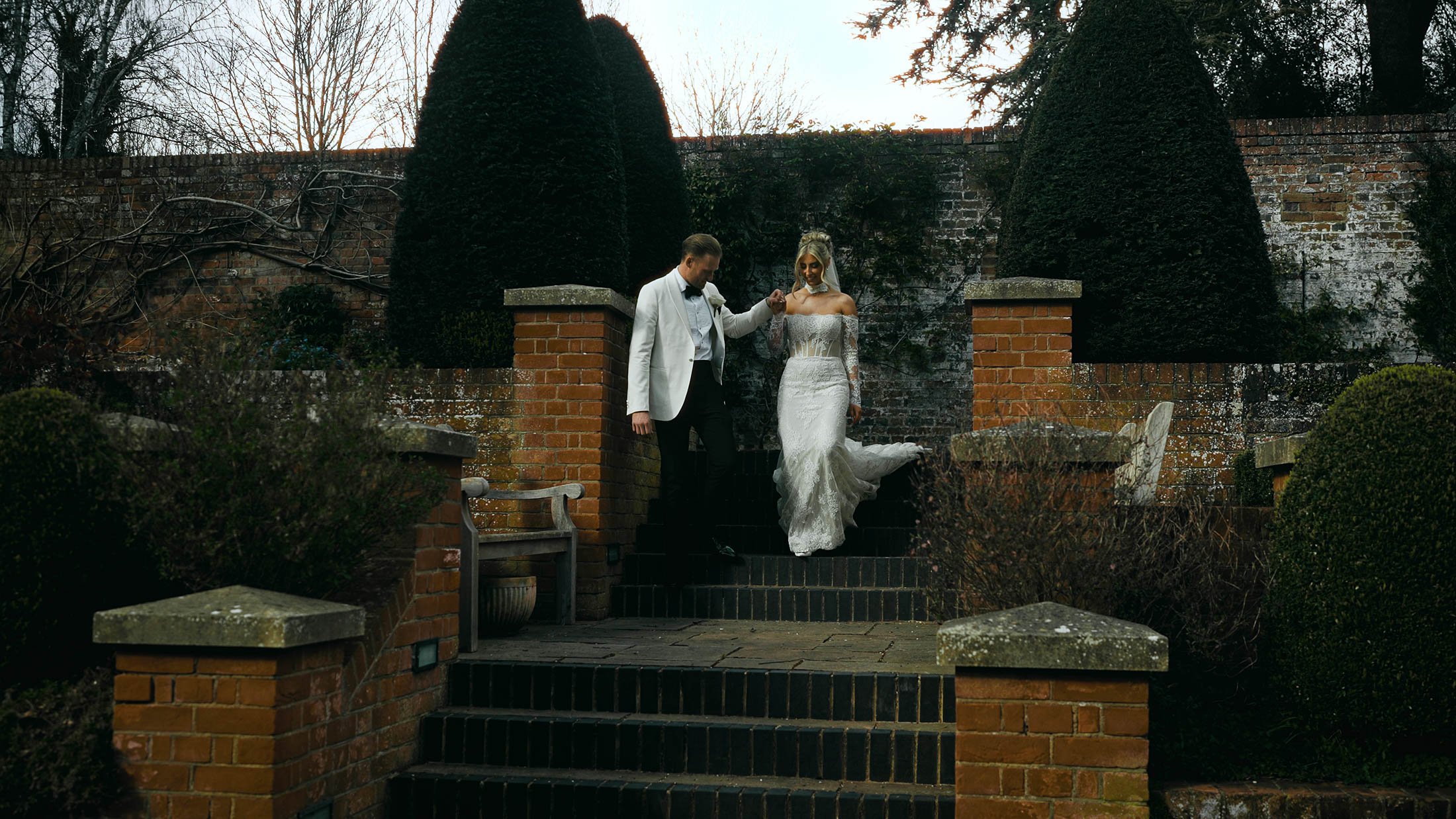 A groom leads his bride down stone steps by the hand in an elegant moment from their storytelling wedding film.