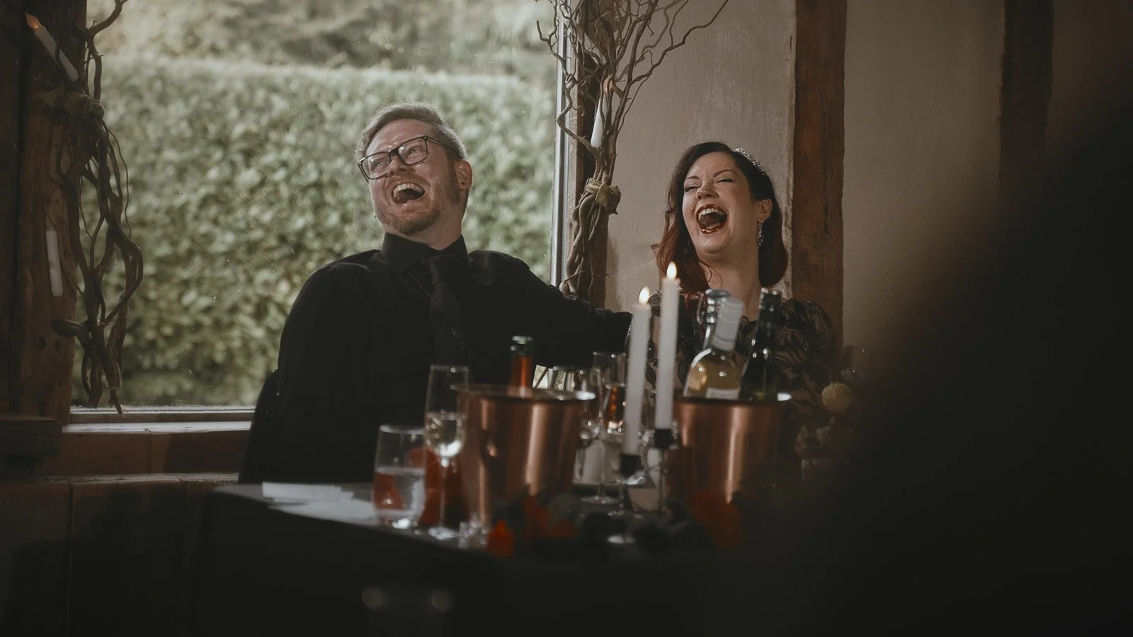 A couple laugh heavily during emotional wedding speeches in the main barn at Winters Barns, Kent.