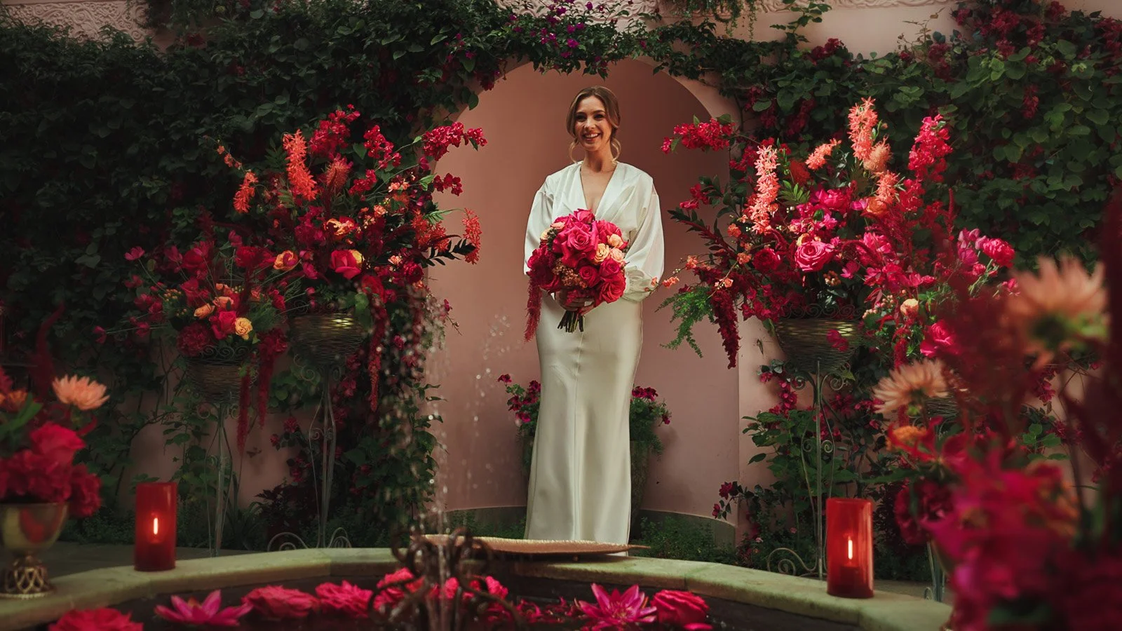 Bride in an elegant minimal dress framed against bold pink and red florals in a fine art composition