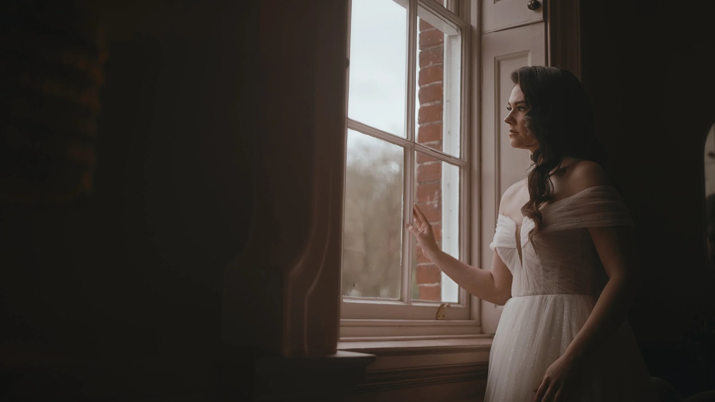 A bridal portrait of the bride looking out of the window in the Wisteria Suite at The orangery, Maidstone during her wedding morning, as she is lit by natural light.