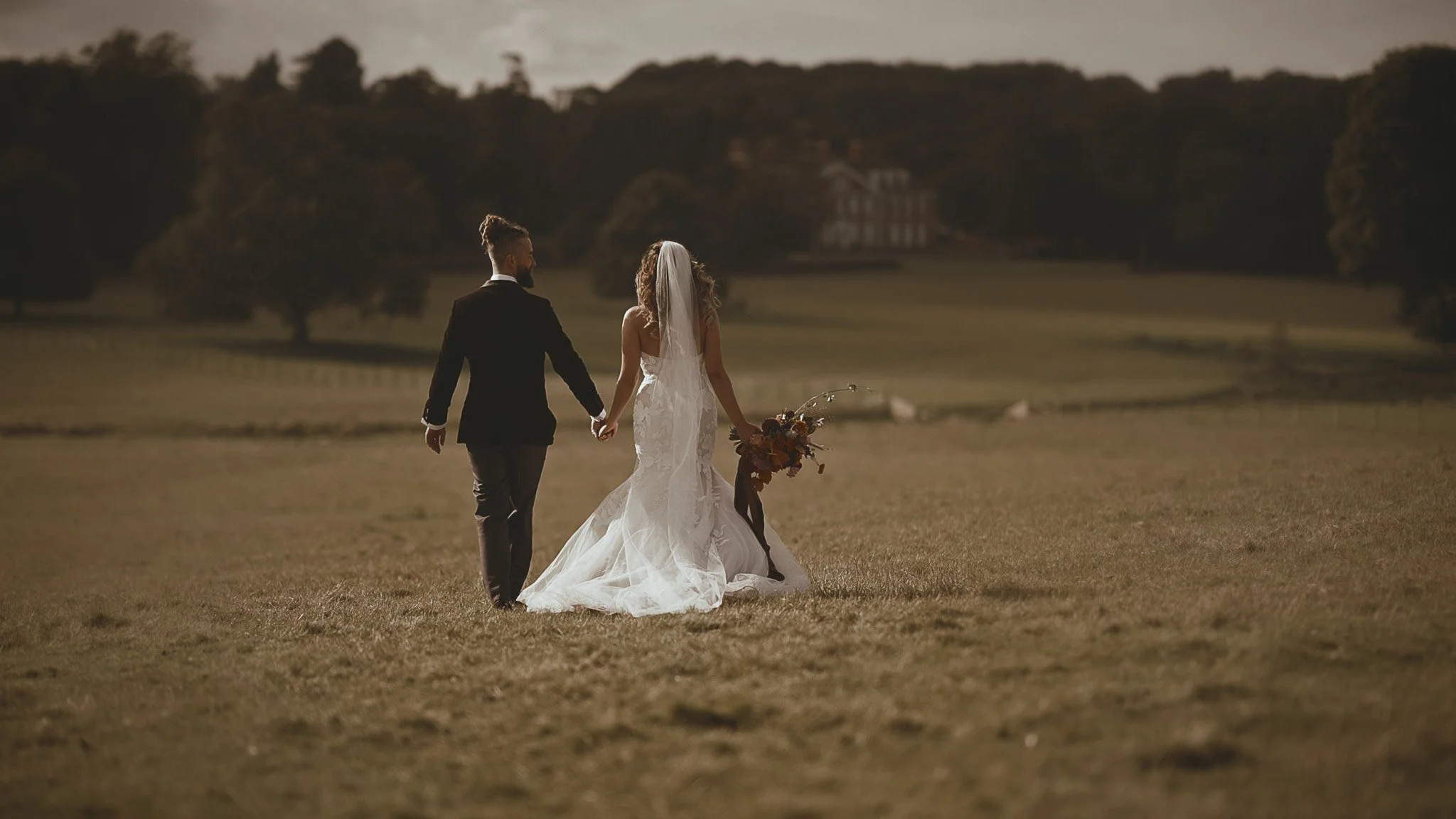 Bride and groom walking away holding hands with rolling countryside surrounding them.