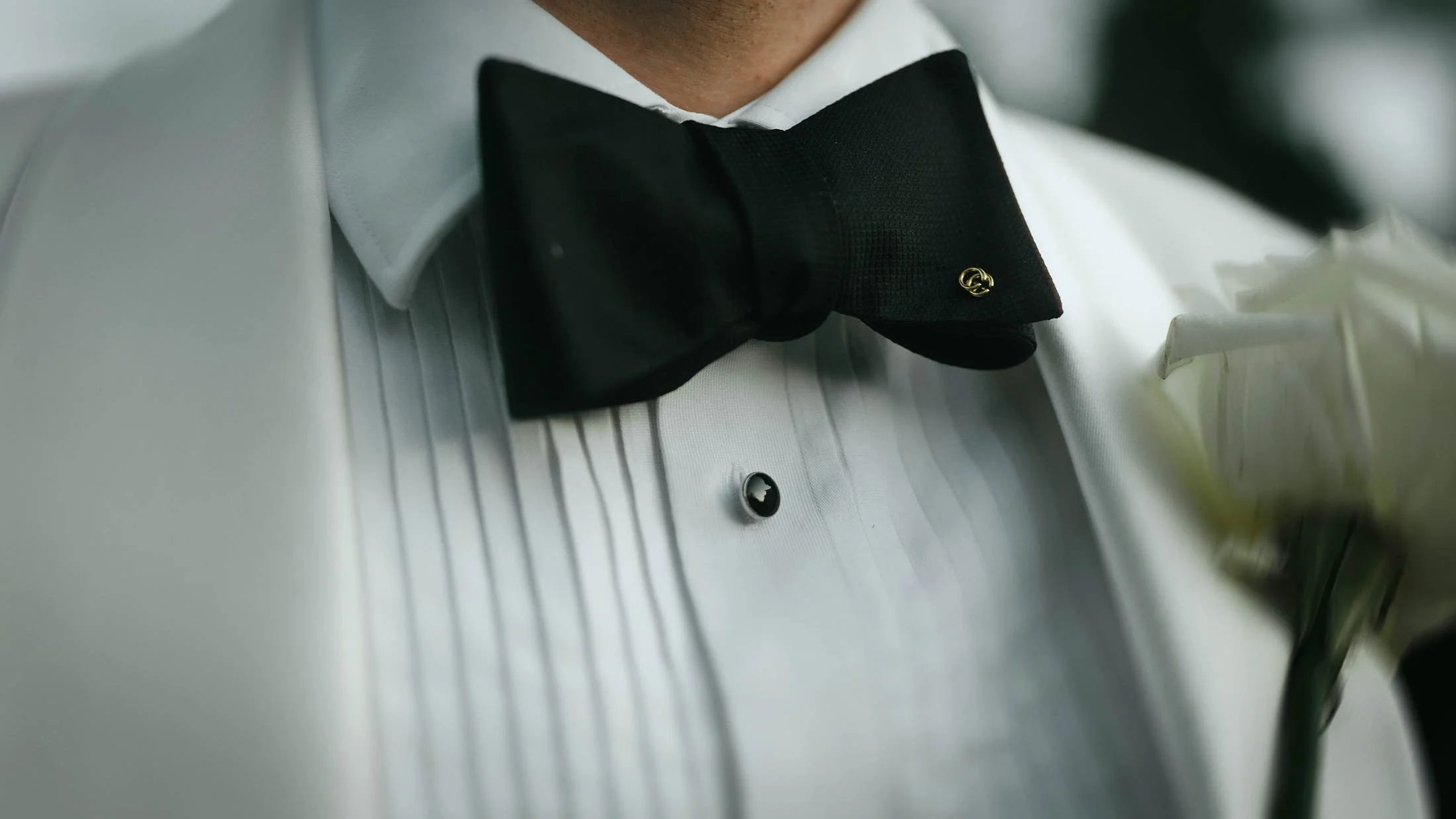 A close-up detailed shot of a black-tie grooms' bow tie with Gucci pin.