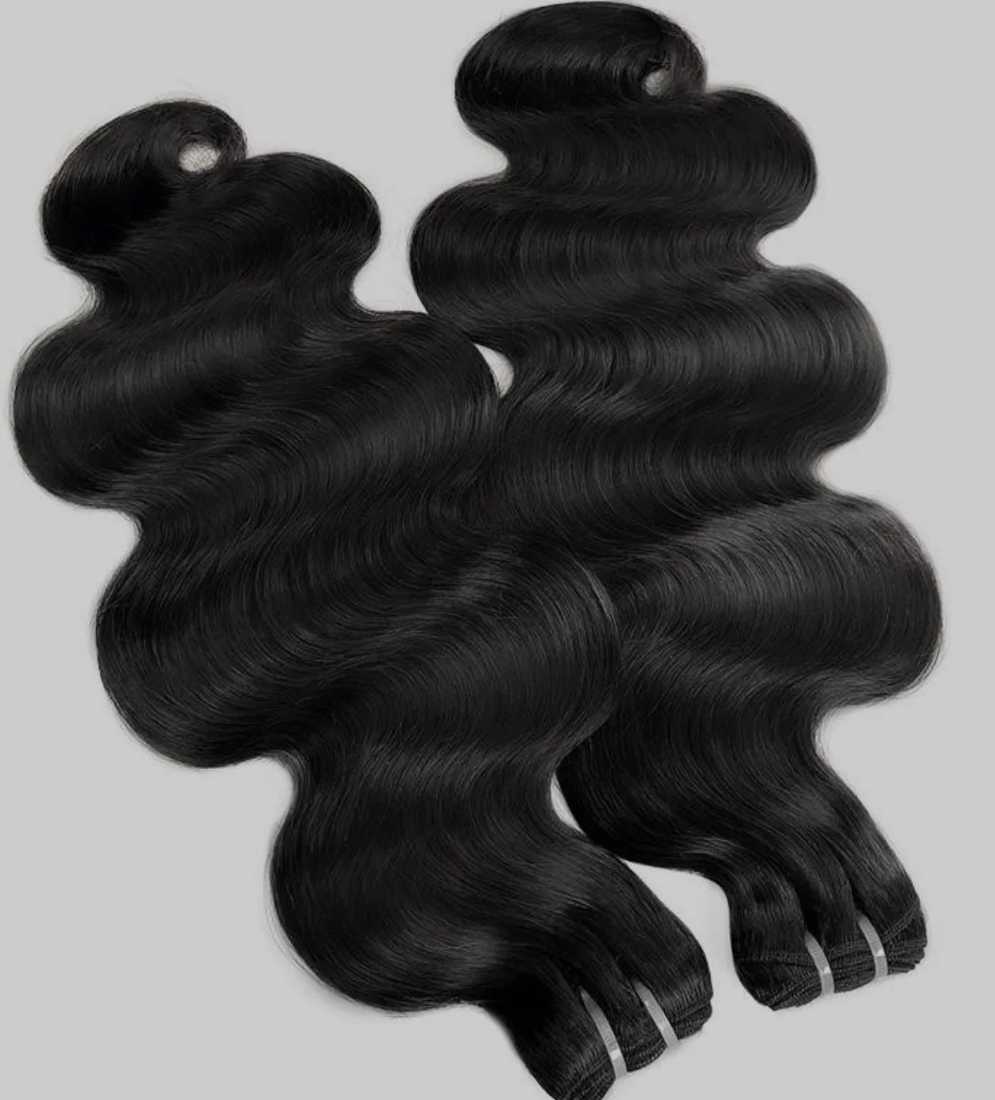 Two bundles of black wavy hair extensions on a gray background.