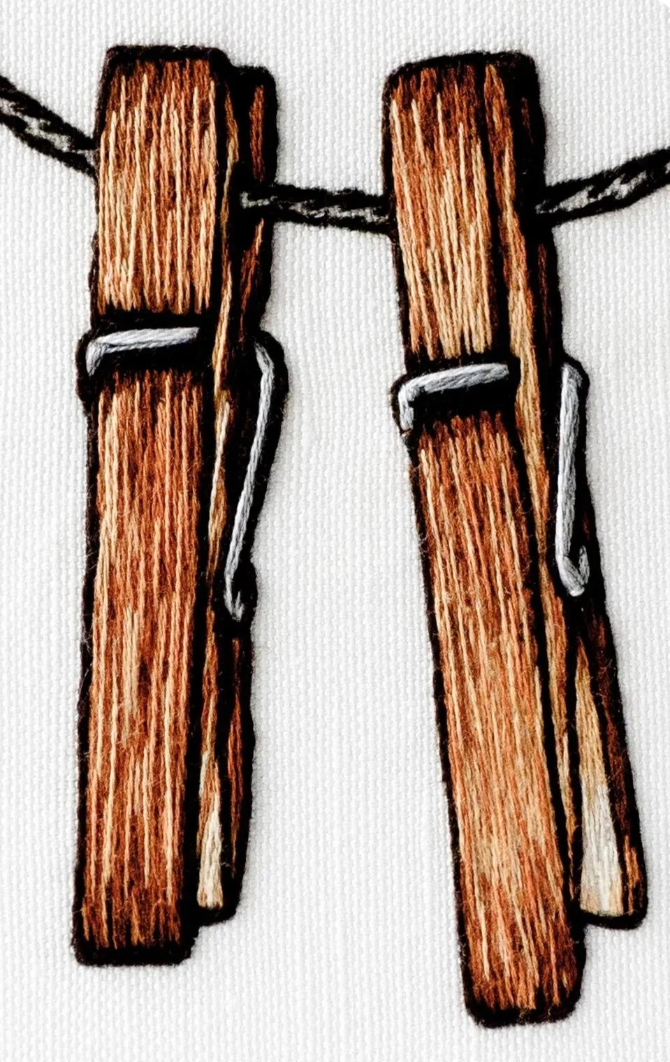 Embroidery of two wooden clothespins hanging on a black thread.