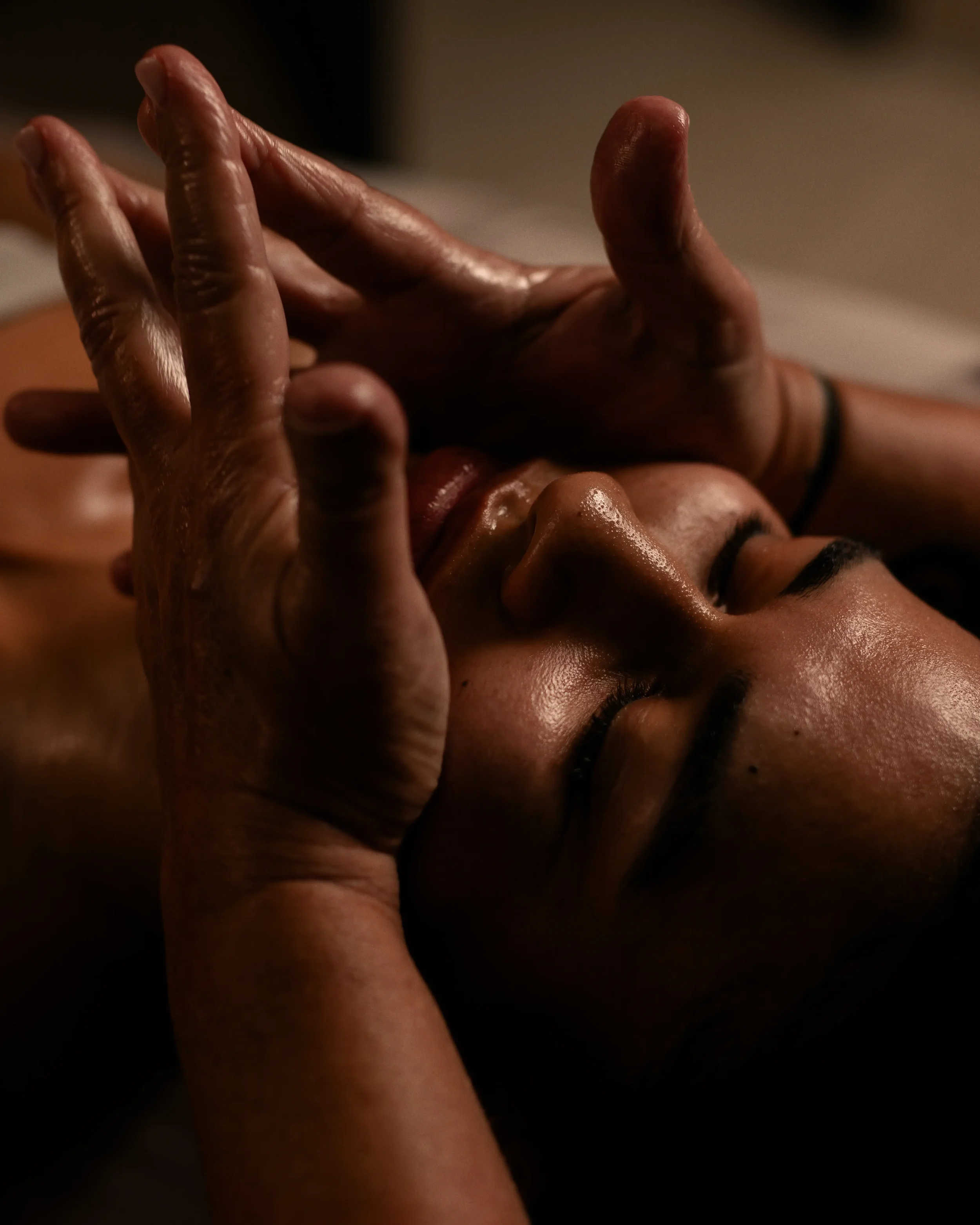 Person receiving a face massage or facial close-up, with eyes closed, hands gently touching the face.