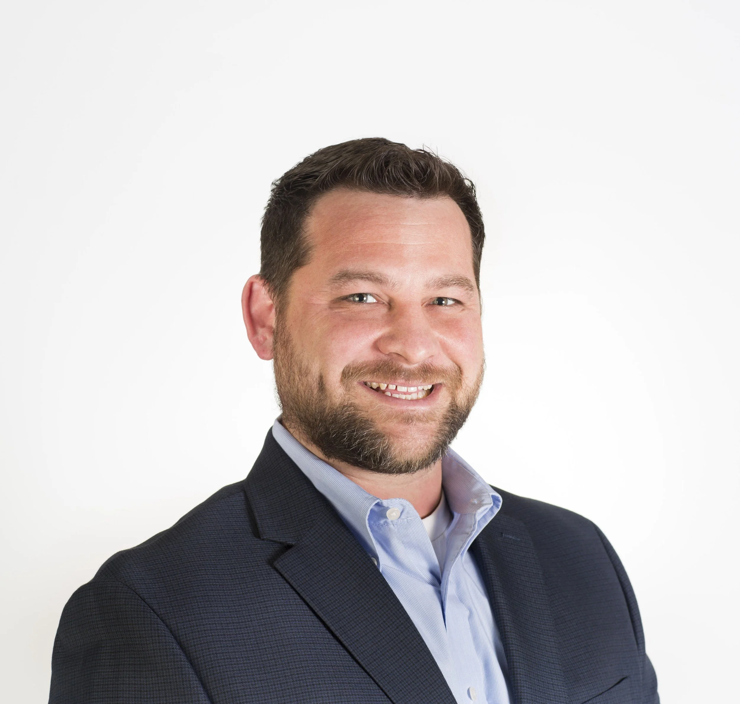 Professional portrait of Ralph Watkins with short dark hair and a beard, wearing a suit jacket and collared shirt, looking confidently at the camera.