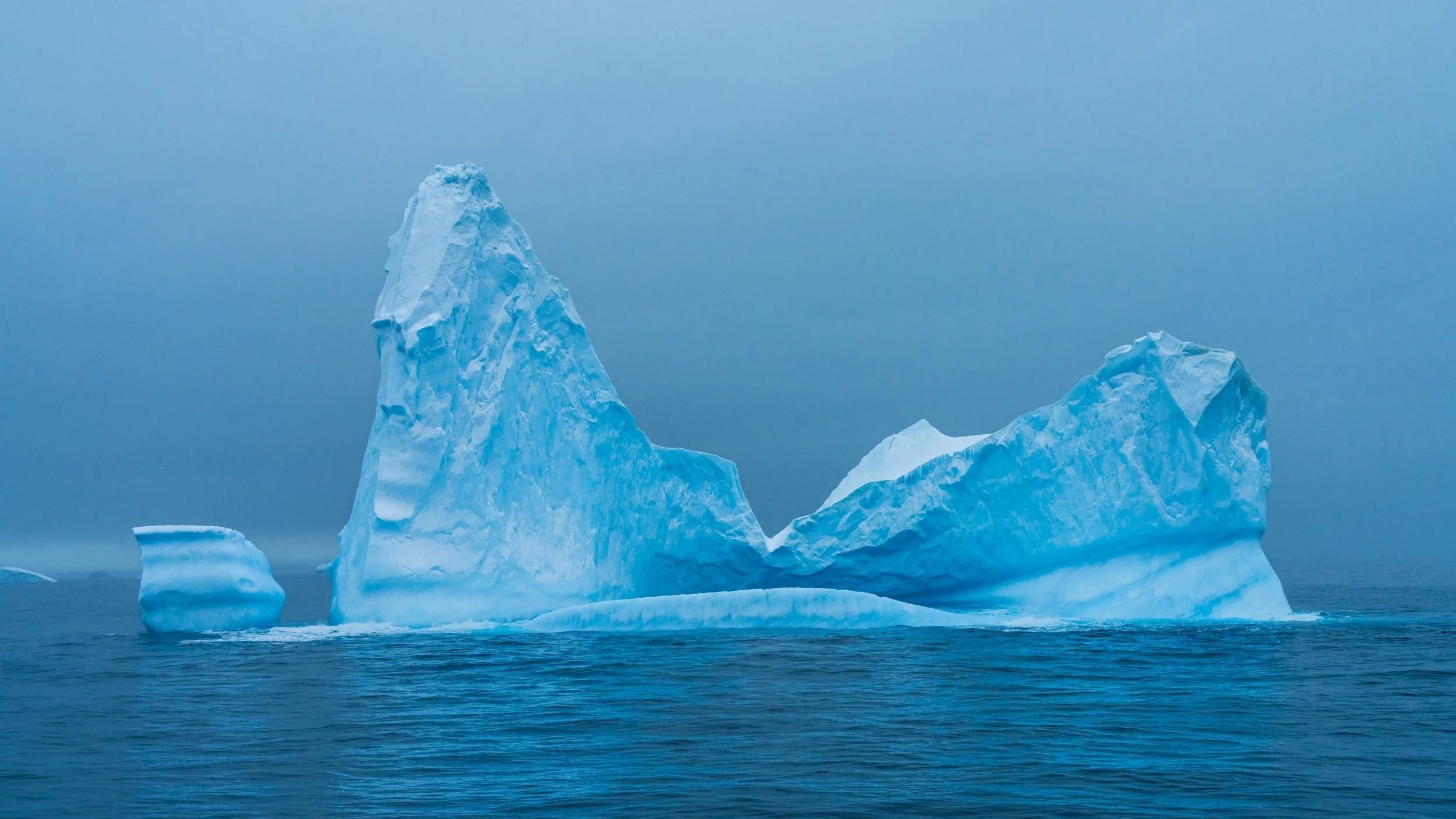A large iceberg floating in the ocean with a cloudy sky in the background.