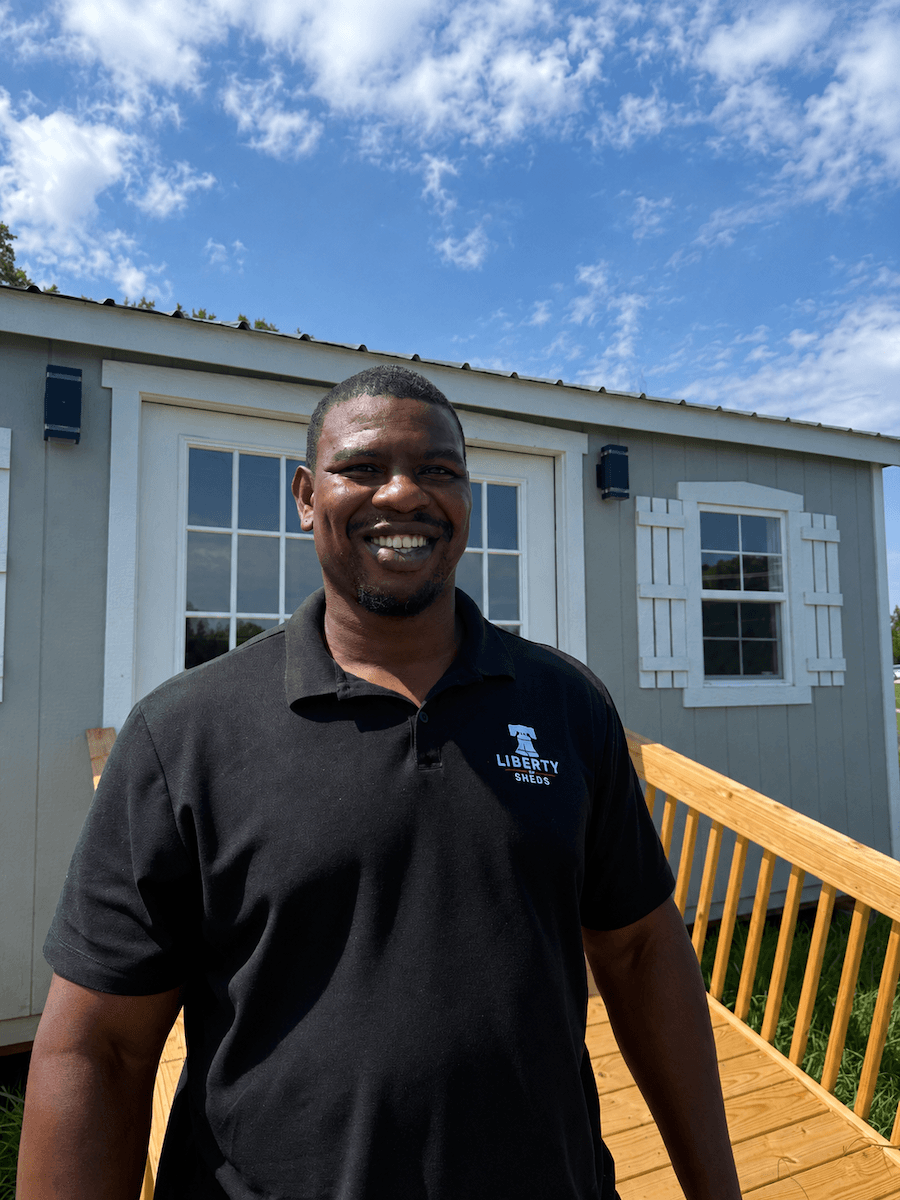 Elijiah, the Liberty Sheds Consultant standing in front of the gray office with white french doors,