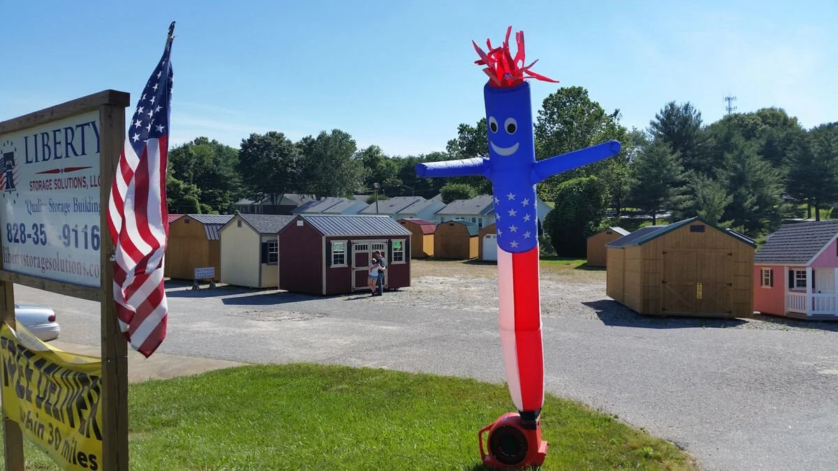 Liberty Sheds Taylorsville lot with American flag style wavy man in front of sheds.