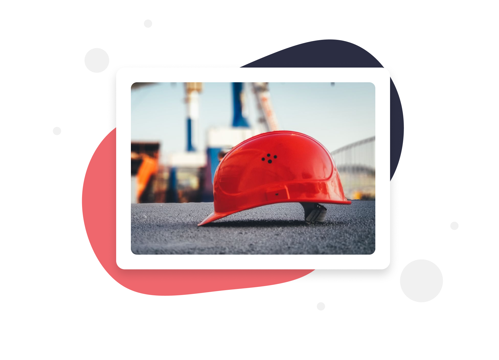 Health & Safety training - Red construction helmet placed on a gray surface outdoors with blurred industrial structures in the background.