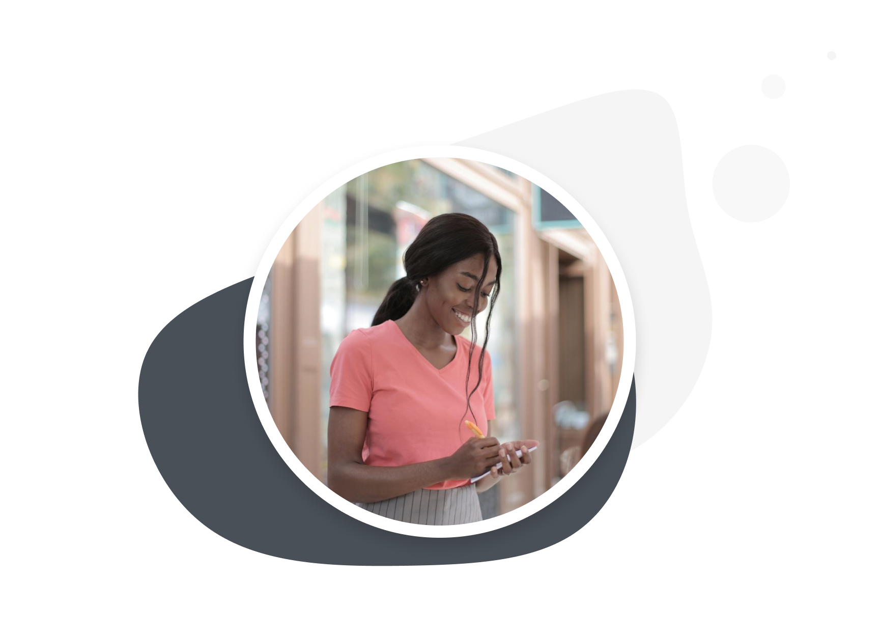 Young woman with long dark hair smiling and looking at her phone while writing on it with a stylus, standing indoors near large windows.