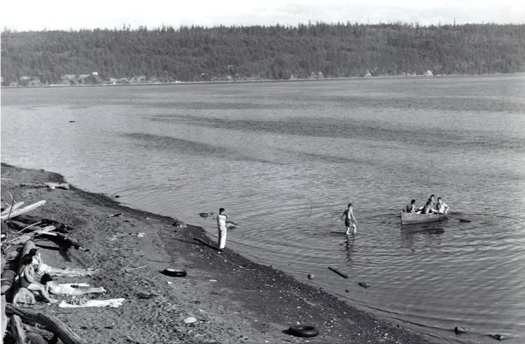 Historical black and white of beach on Discovery Bay with sunbathers and boat and people on the water