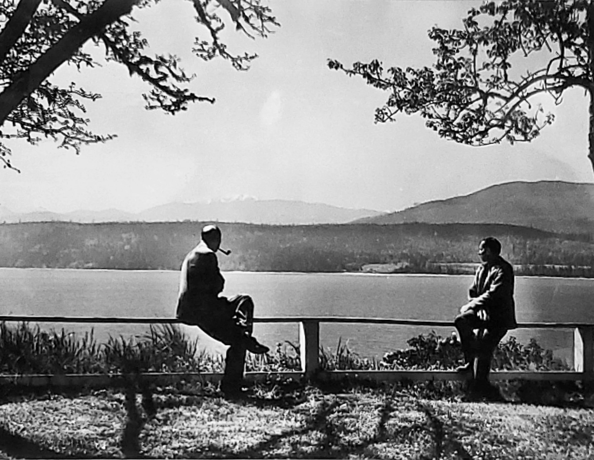 Historical black and white of two men sitting on the fence by Discovery Bay at Chevy Chase Beach Cabins