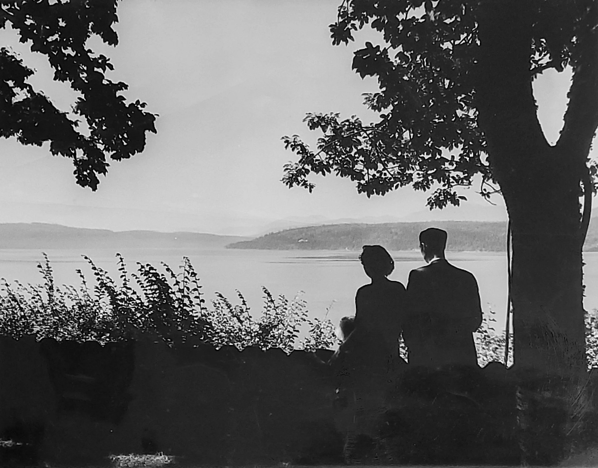 Historical black and white of silhoette of couple by the bay with a tree to the right 