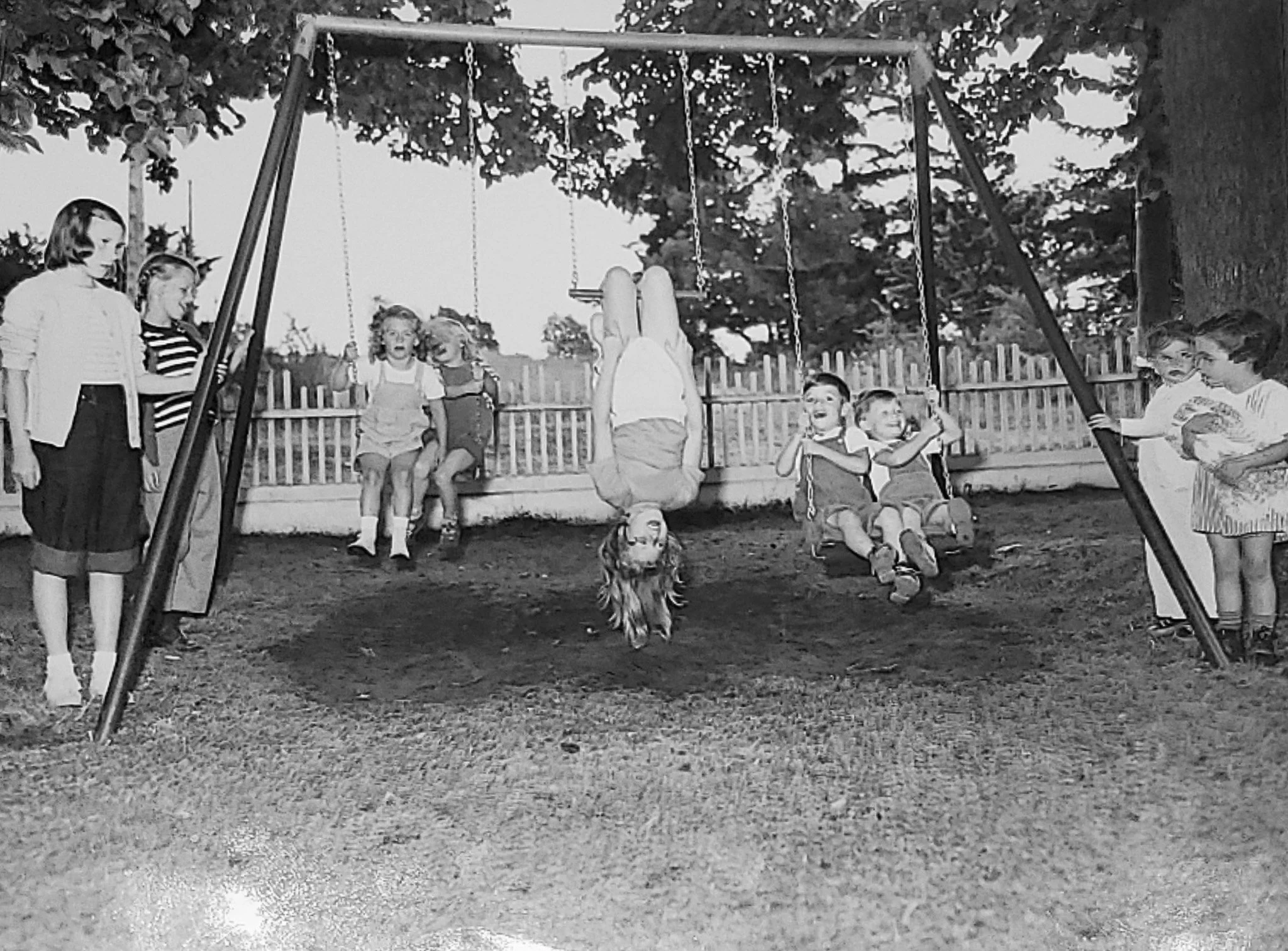 Historical black and white of nine kids playing on and around swingset