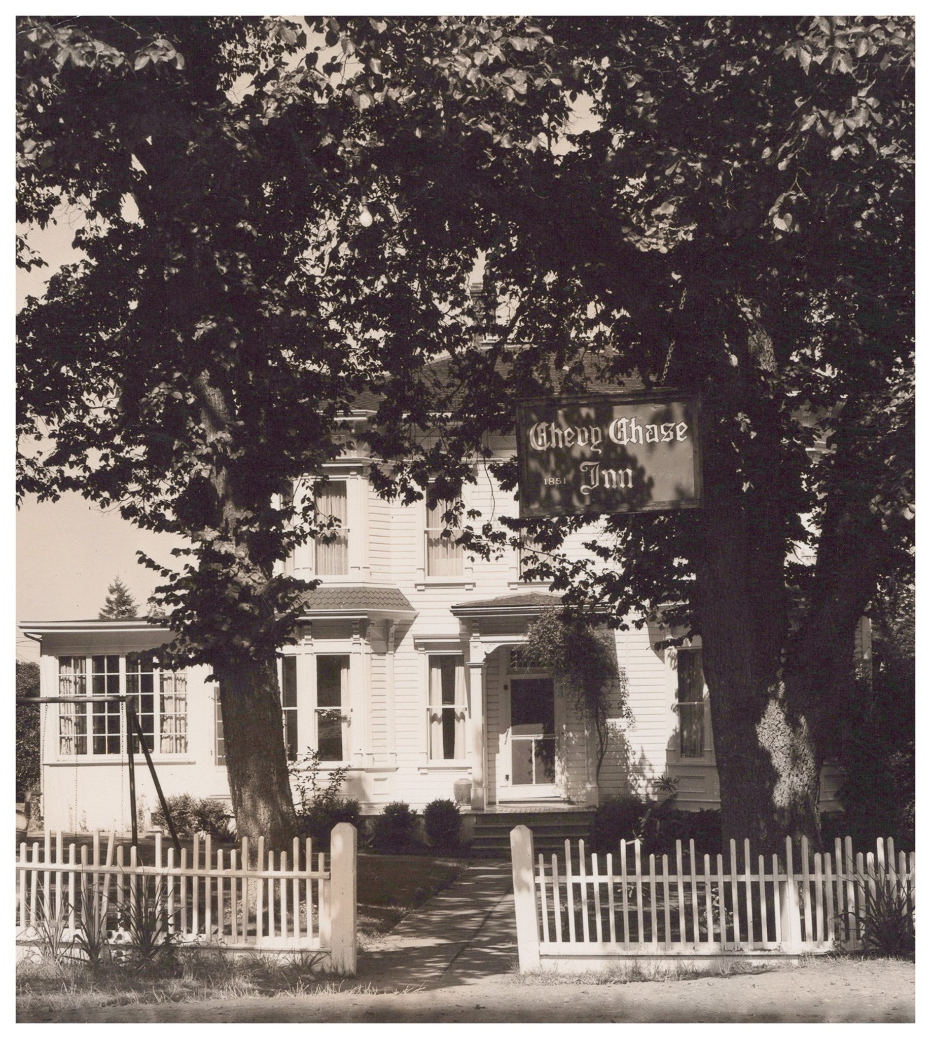 Historical black and white of Chevy Chase Inn with white picket fence and large elm trees
