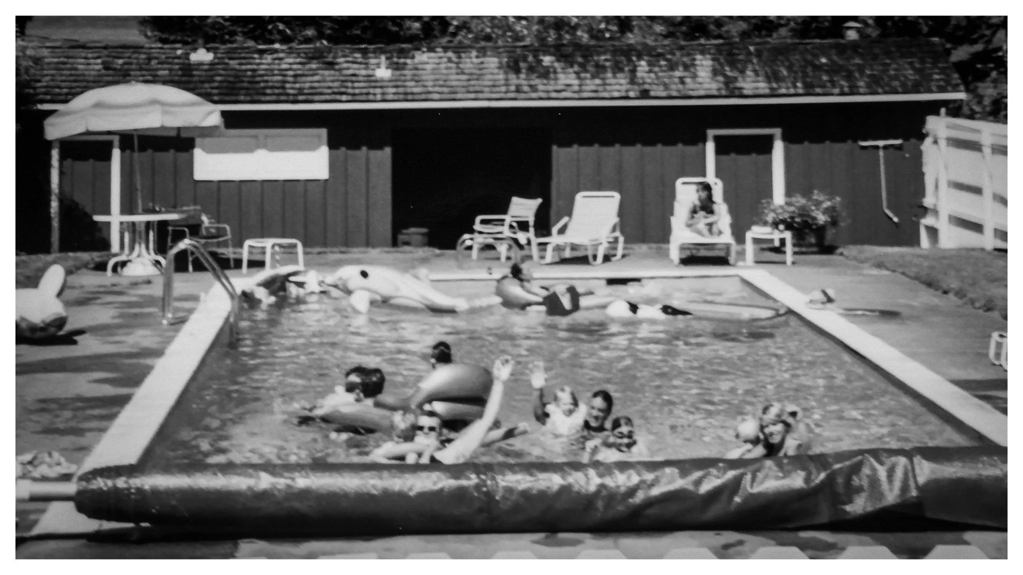 Historical black and white of people swimming in the pool in front of the pool house