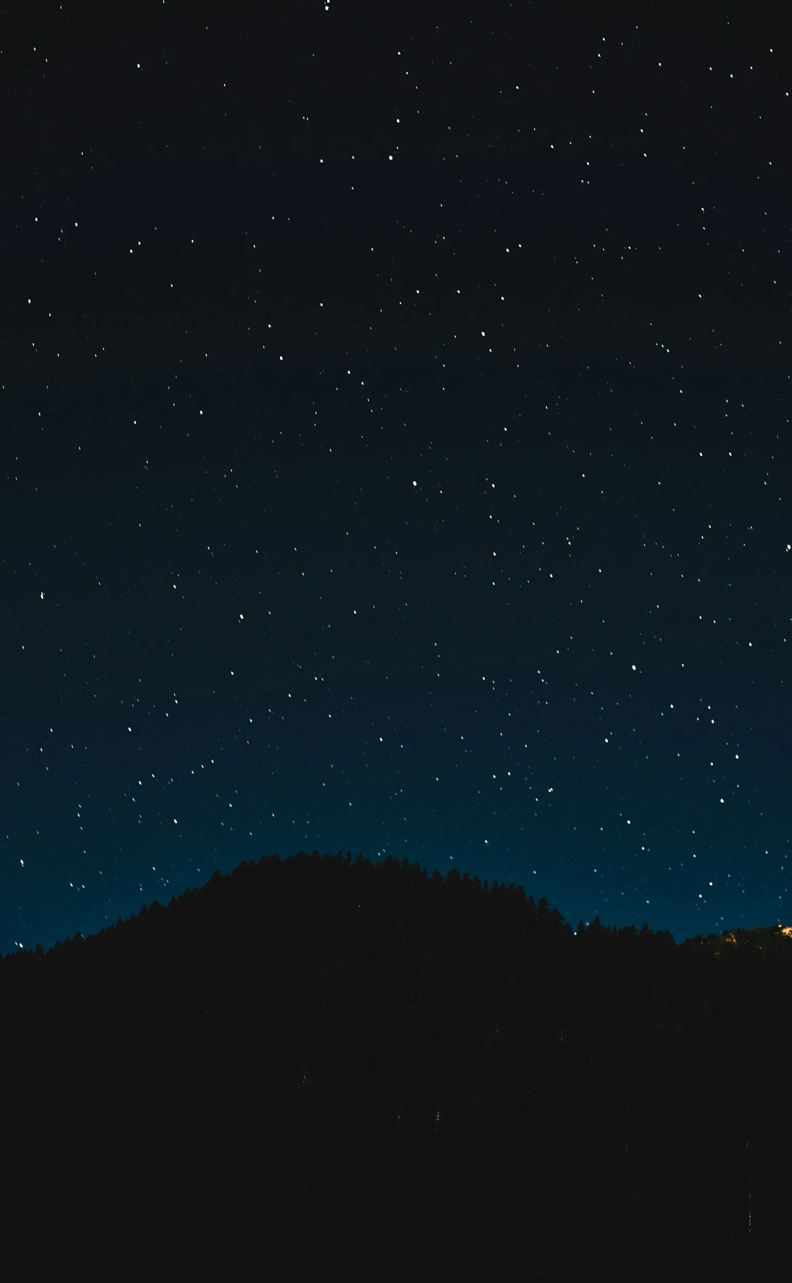 Night sky with stars over a silhouette of trees and a hill.