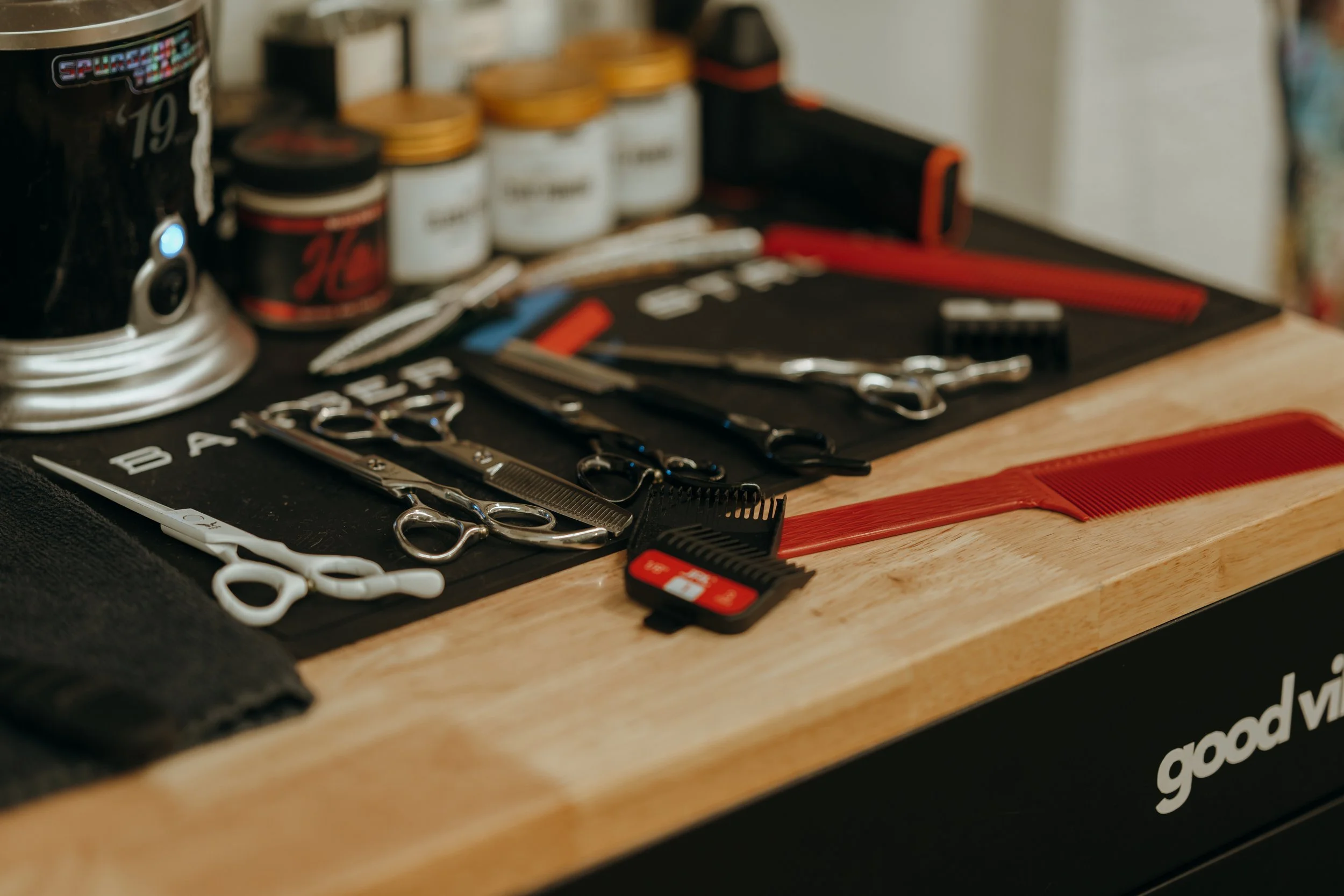 A wooden table with various haircutting tools including scissors, a comb, and hair clips, alongside hair styling products and a small toolbox.
