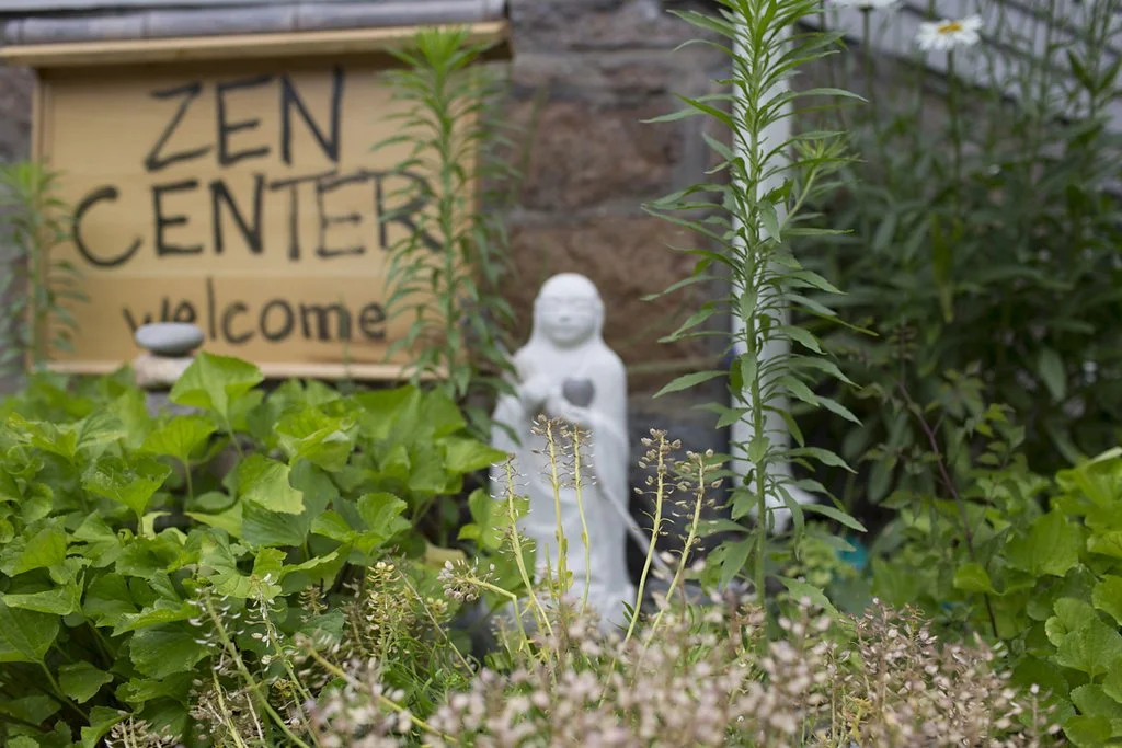 Small statue standing in front of a sign that reads zen center welcome