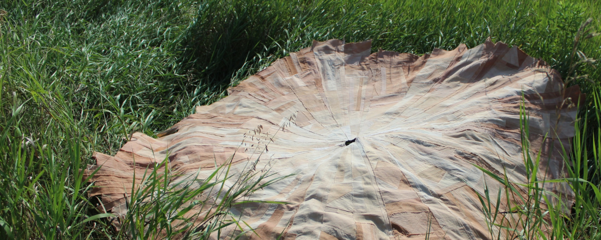 An intricately pieced circular textile art piece created by artist Maggie Dimmick rests on green grass