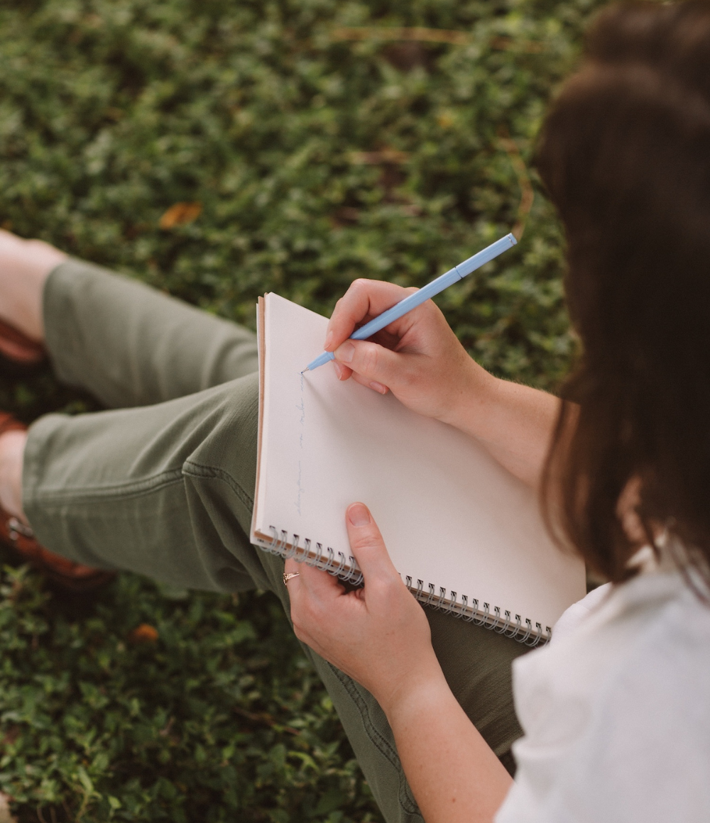Rebecca Magee is pictured writing in a notebook while sitting in the grass