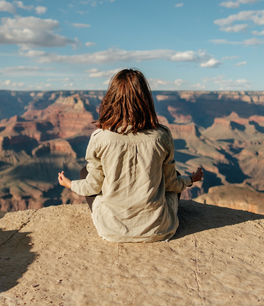 A woman sits in contemplation on a rock, overlooking a wide canyon