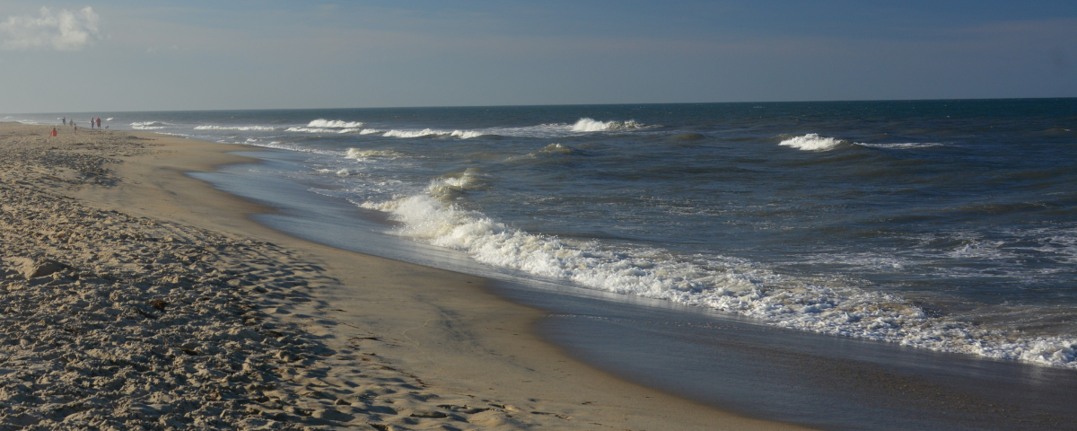 Waves roll onto the shores of a North Carolina beach as people walk in the distance