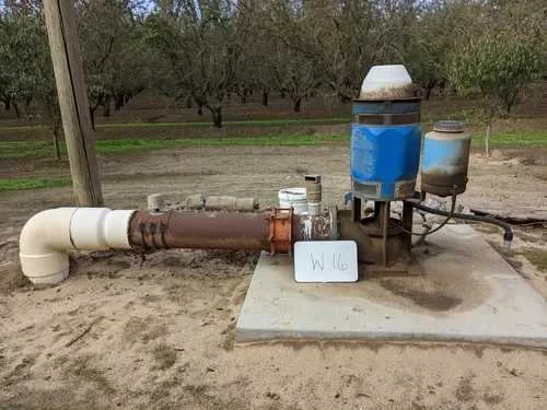Irrigation pump system with pipes and blue motor in an orchard setting.