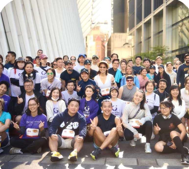Garden of Hope New York Photo of a large group of diverse people gathered outdoors in an urban setting, many wearing running gear and bib numbers, smiling and posing for a group photo.
