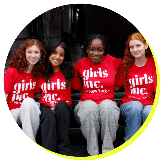 Four diverse young women sitting on stairs wearing matching red t-shirts that say "Girls Inc. of New York" and smiling at the camera.