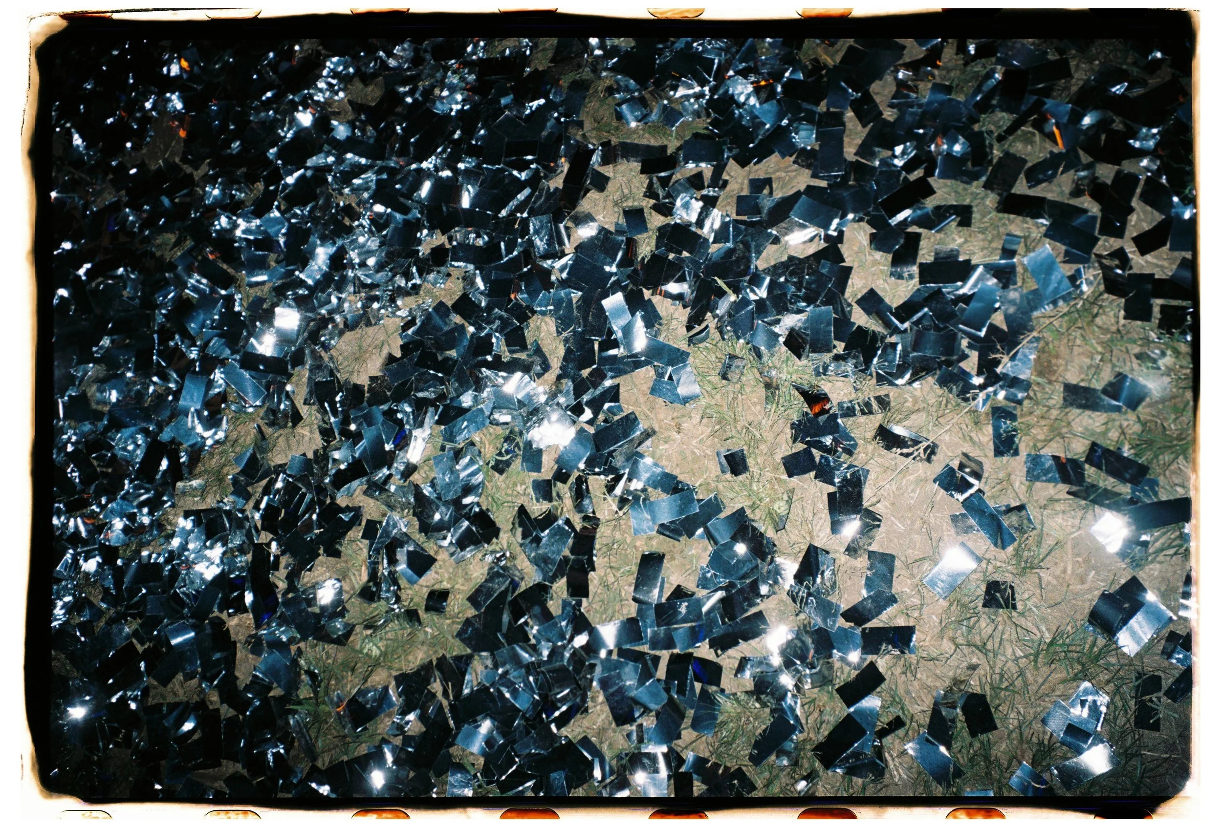 Fragmentos de espejo dispersos sobre césped, reflejando la luz.