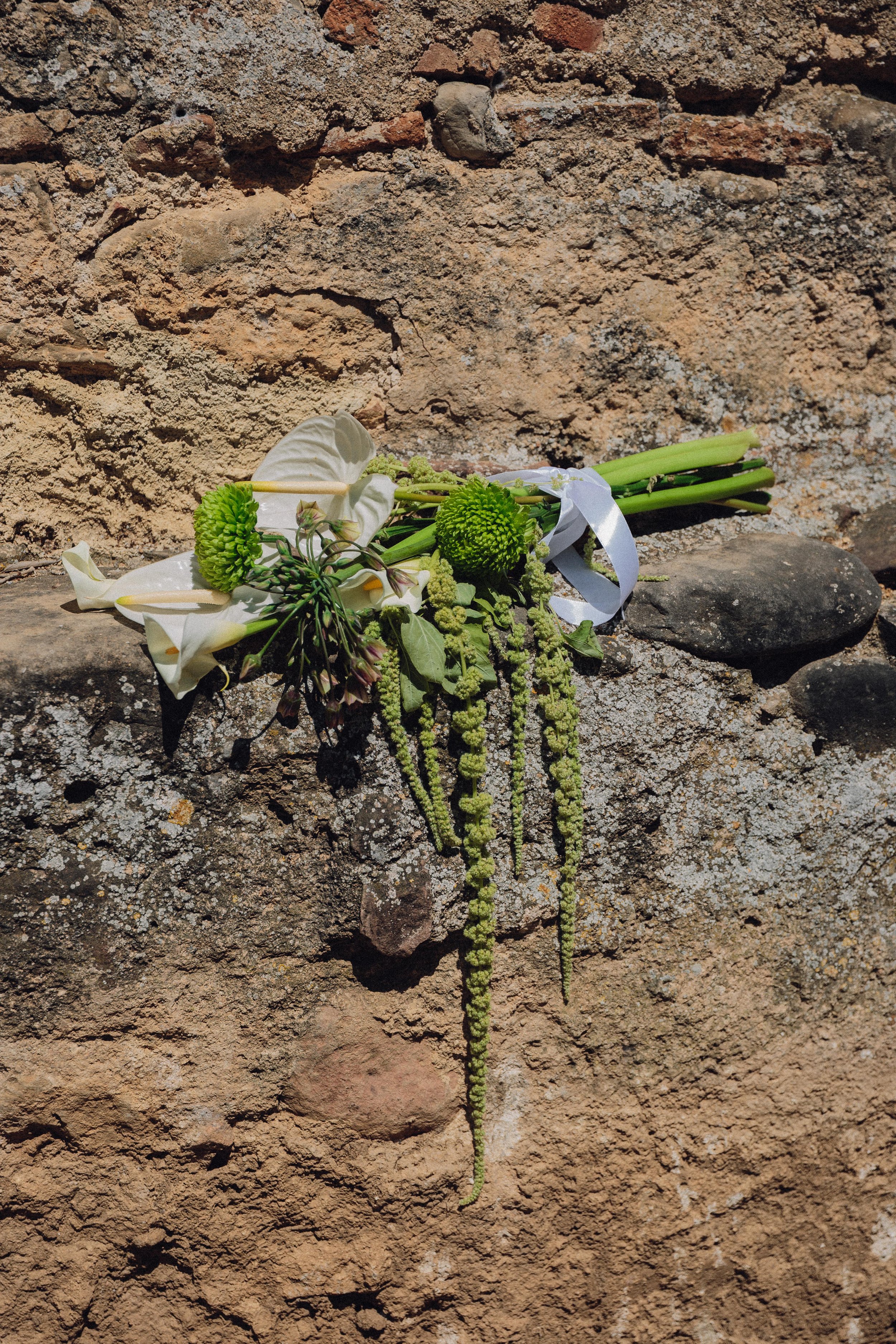 Ramo de flores blancas y verdes, colocado sobre una roca, en un muro de piedra.