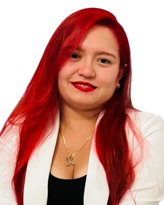 A woman with long red hair, wearing a white blazer and a black top, smiling at the camera.