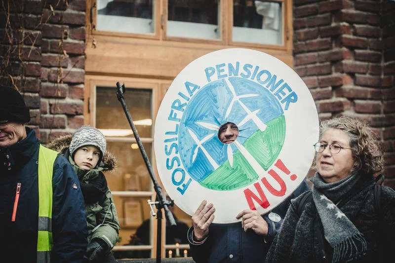 En kvinna håller upp en skylt med texten "Fossilfria pensioner nu" och bilder på vindsnurror.