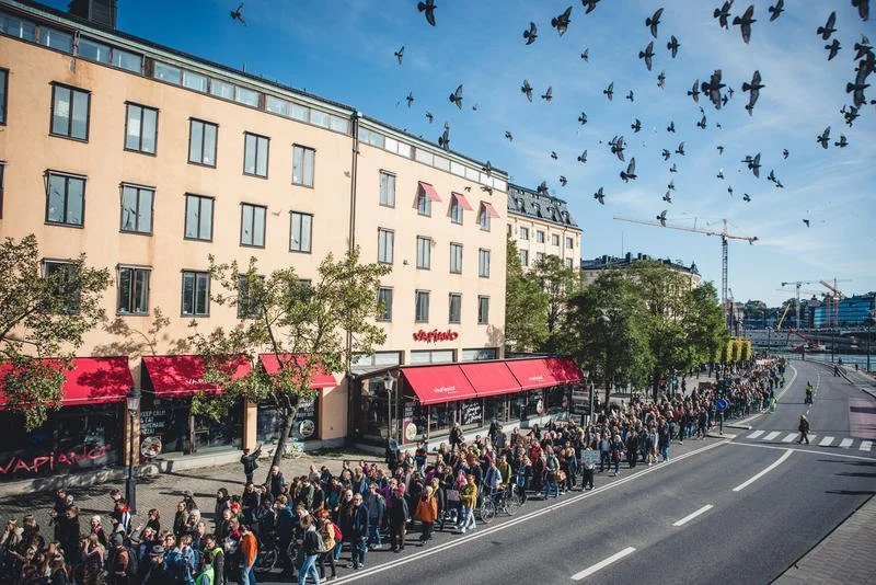 Ett demonstrationståg går i stadsmiljö på sommaren och duvor flyger ovanför.