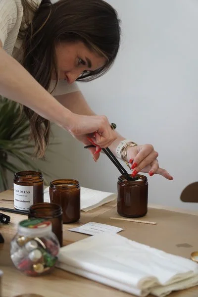 A woman using tongs to pick up a small item from a dark amber jar on a table.