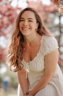 Smiling young woman with long wavy hair outdoors near pink blossoming trees