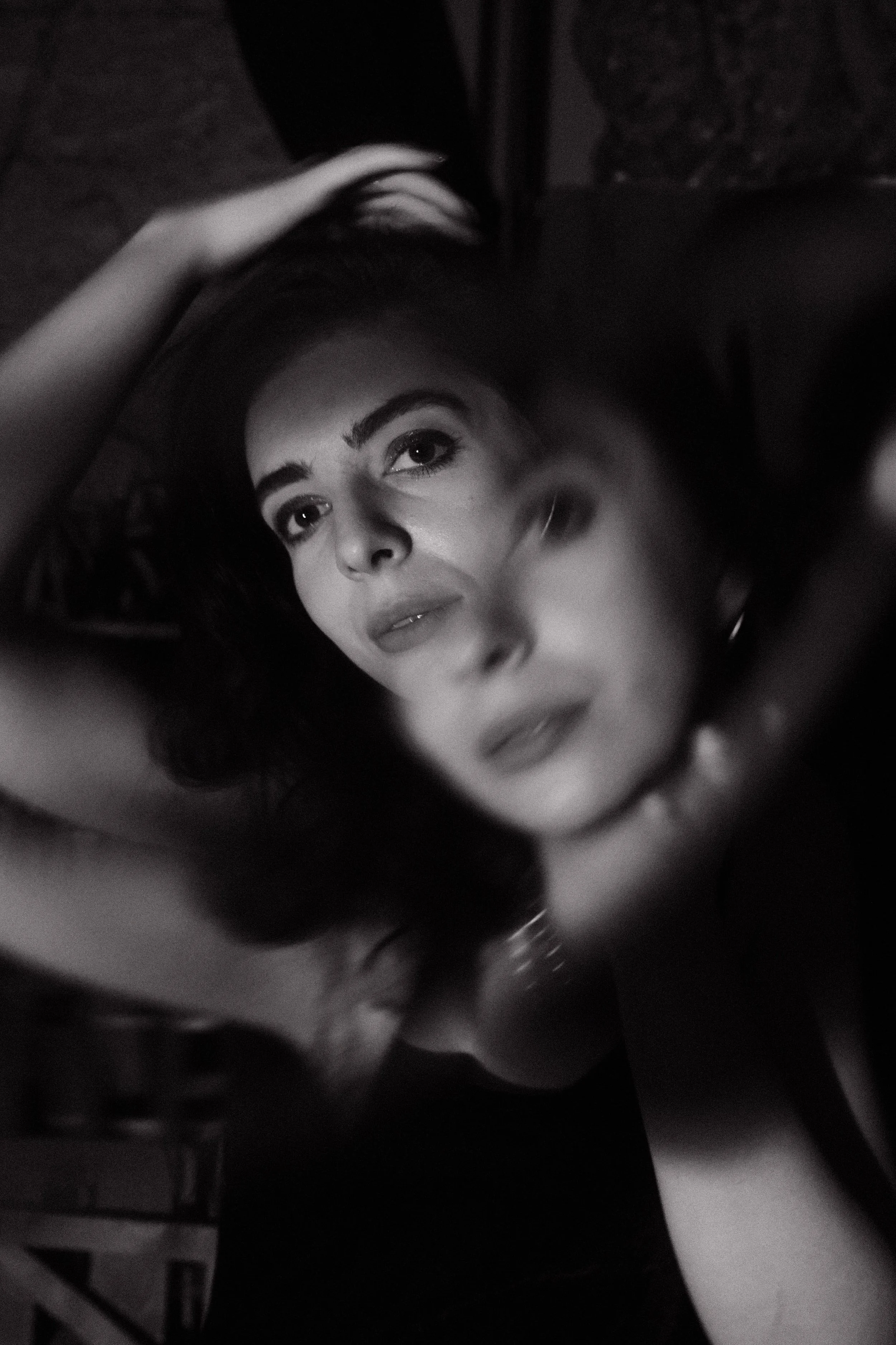 Black and white photo of a woman with long dark hair lying down, with a hand in her hair, looking up at the camera.