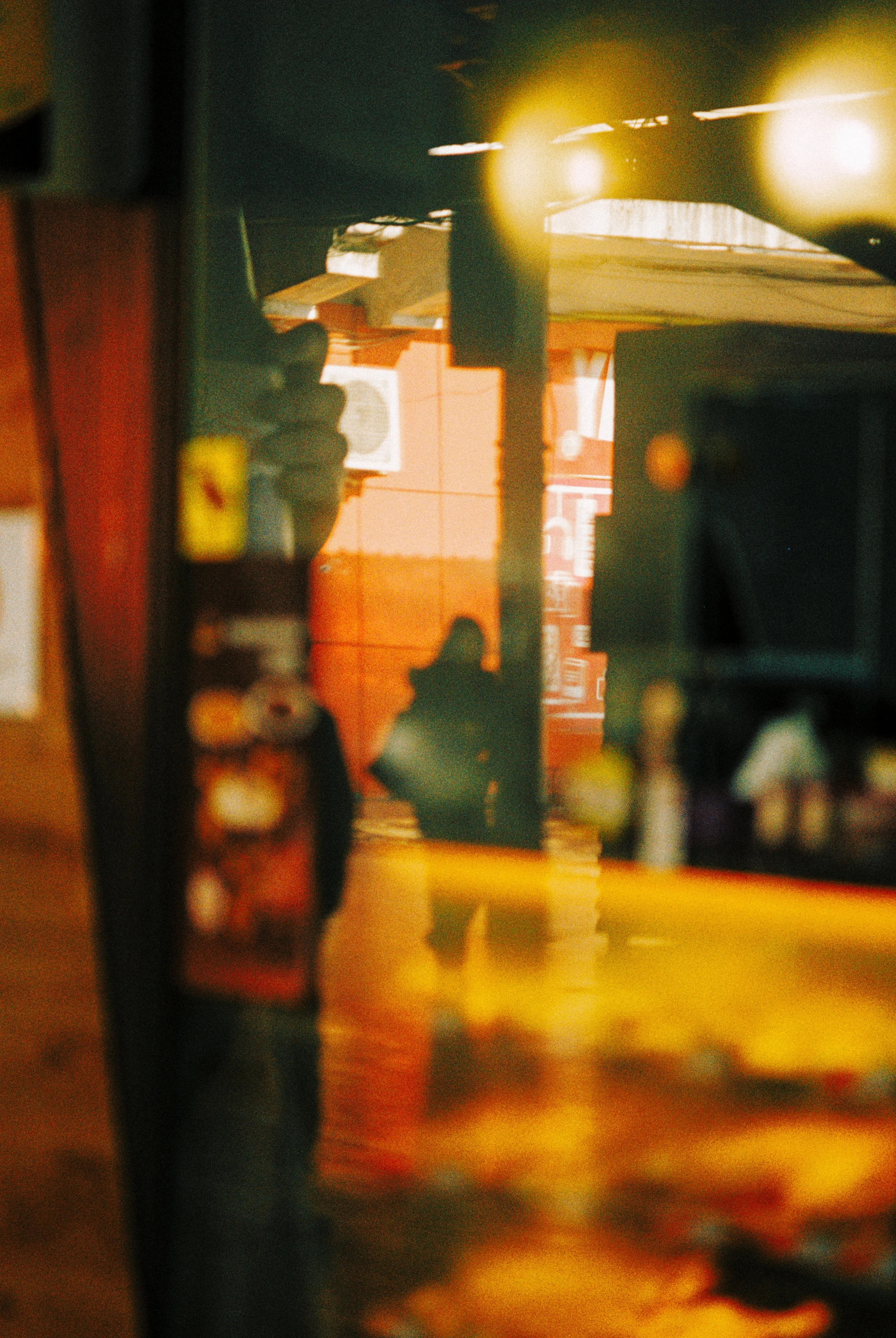 A person taking a photo, with their reflection visible on a glass surface, creating a layered image with warm tones.