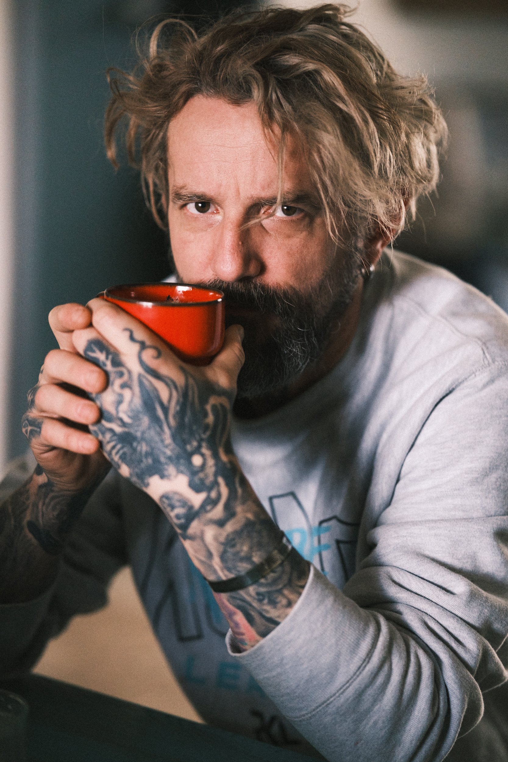 A man with tattoos and a beard, holding a red cup, drinking and looking at the camera.