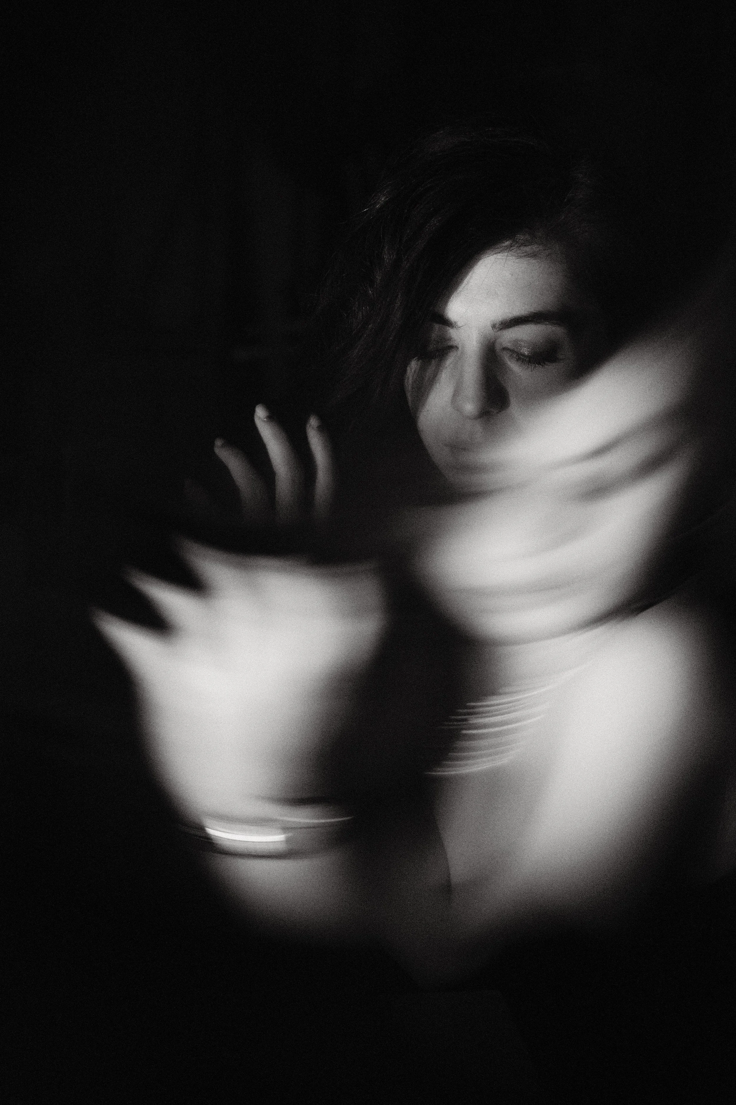 Black and white portrait of a woman with eyes closed, long hair, and a hand near her face, with a blurry abstract background.
