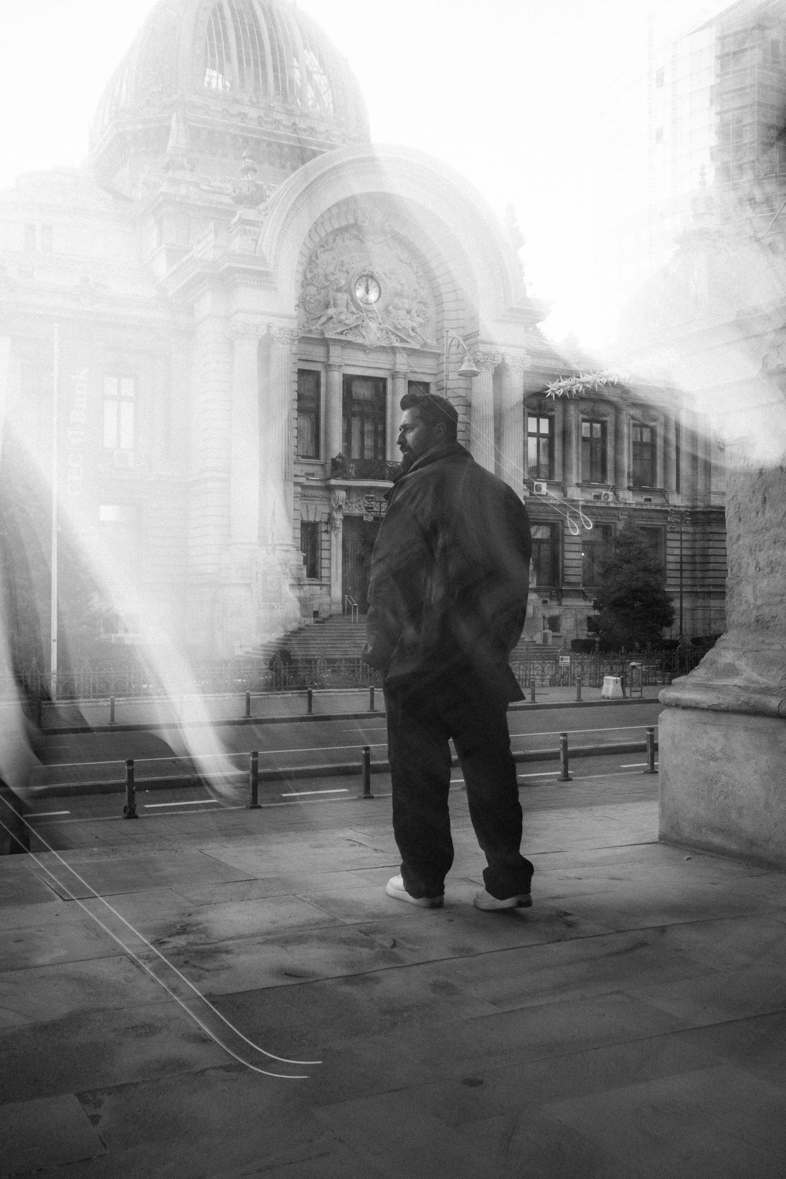 Black and white portrait of Ahmed Hatem reflected in a glass surface, layered with a historic building facade in Bucharest.
