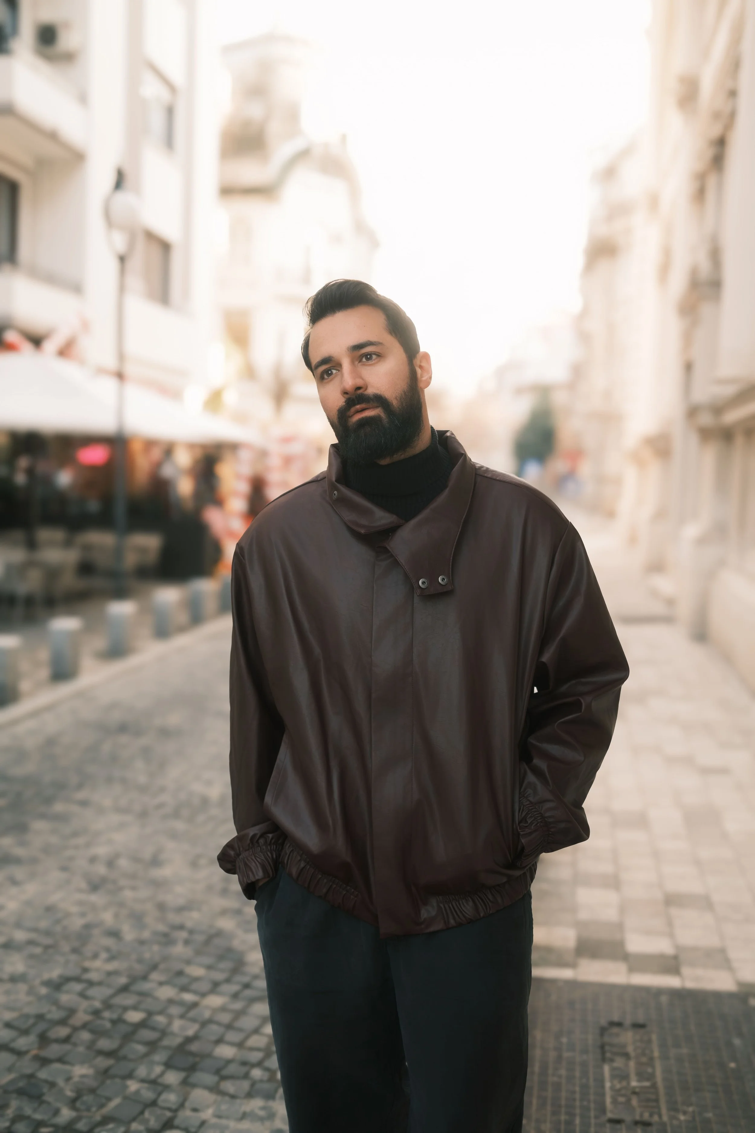 Ahmed Hatem stands on a cobblestone street in Bucharest, wearing a dark leather jacket, surrounded by soft urban textures.
