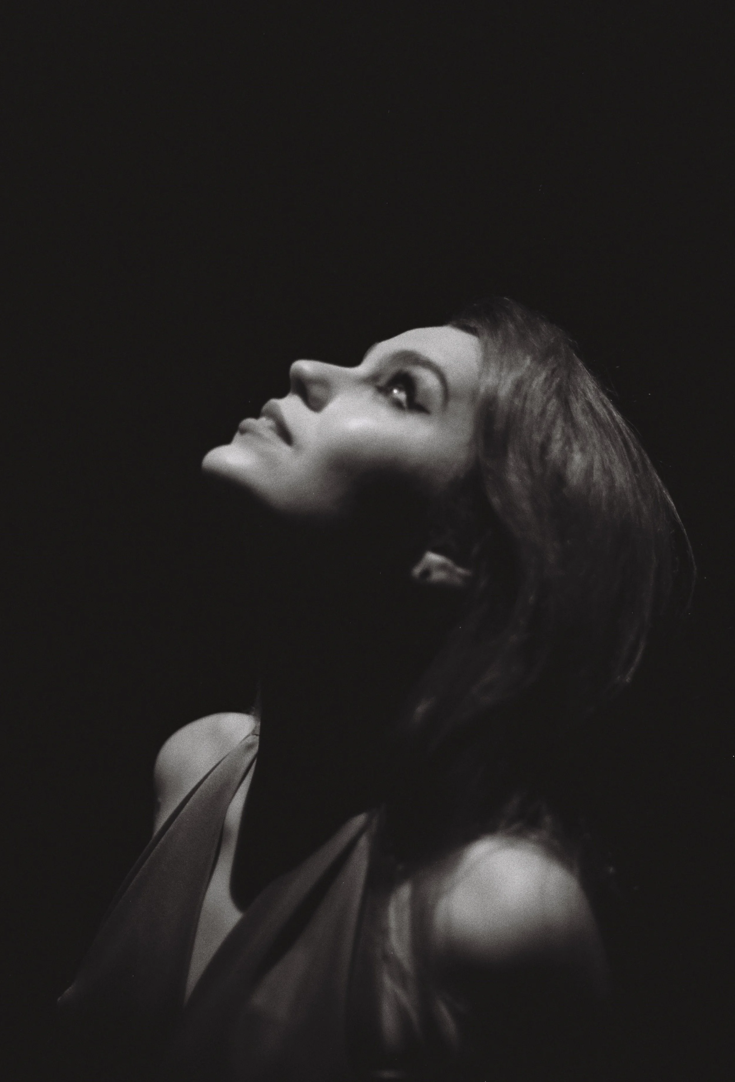 A black and white side profile of a woman looking upward, with soft lighting highlighting her face and hair.